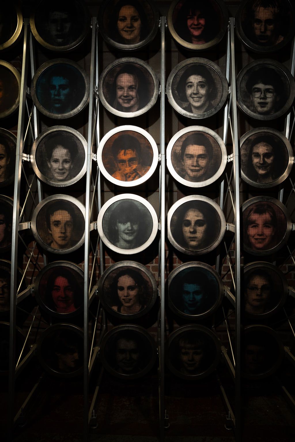 A dark art installation featuring multiple circular frames arranged in rows displaying colorful portrait photographs of various faces.