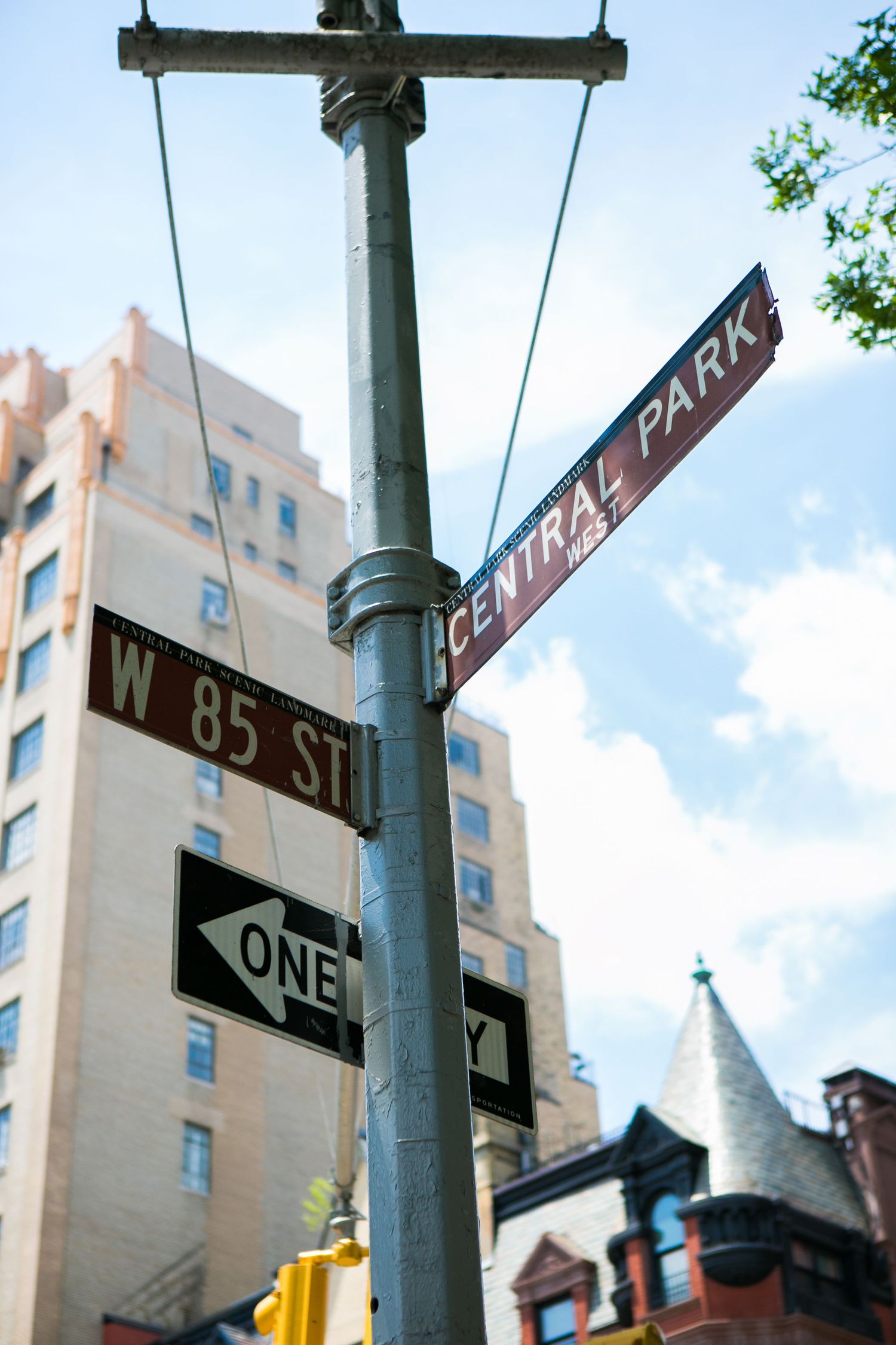 Street signs for West 85th Street and Central Park West in New York City with buildings in the background.