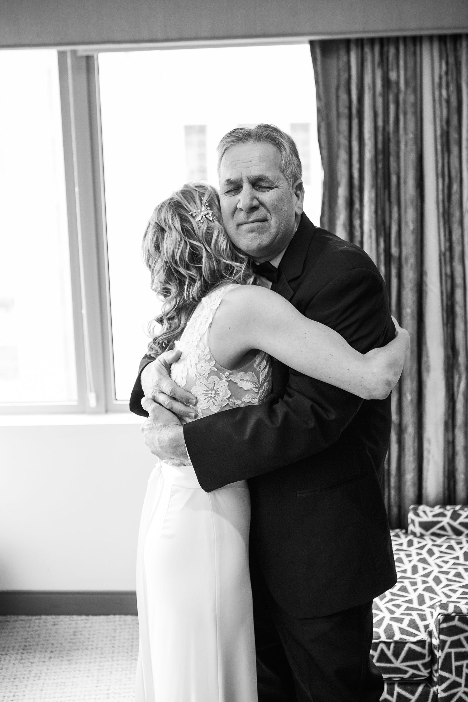 Emotional black and white photo of father hugging daughter in wedding dress before ceremony.
