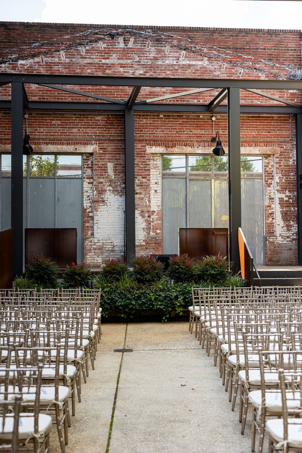 Outdoor wedding ceremony setup with chiavari chairs facing brick wall industrial venue.