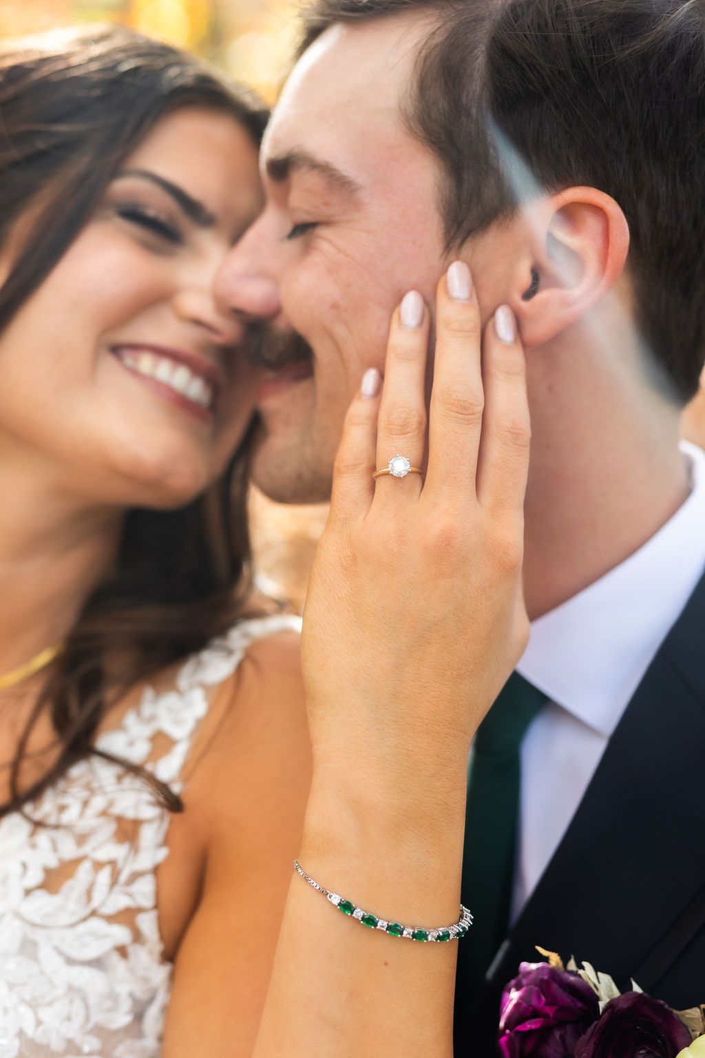 Close-up of bride showing diamond ring and emerald bracelet while smiling beside groom outdoors.