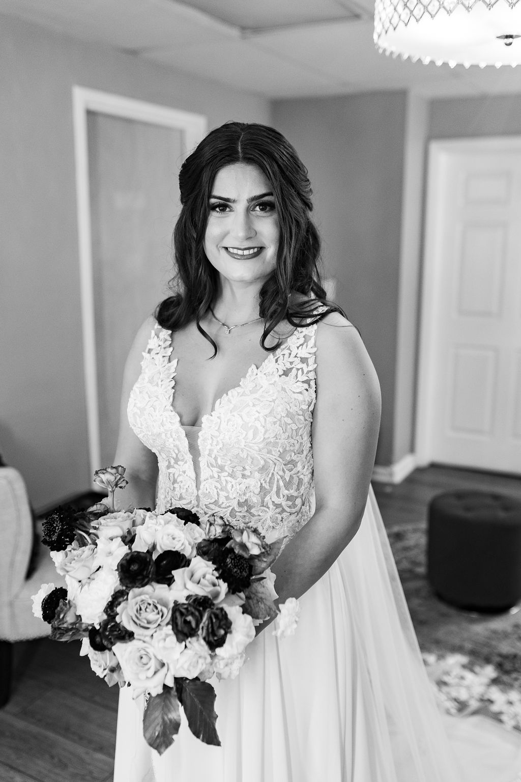Black and white portrait of a smiling bride in a lace wedding gown holding a bouquet of roses.