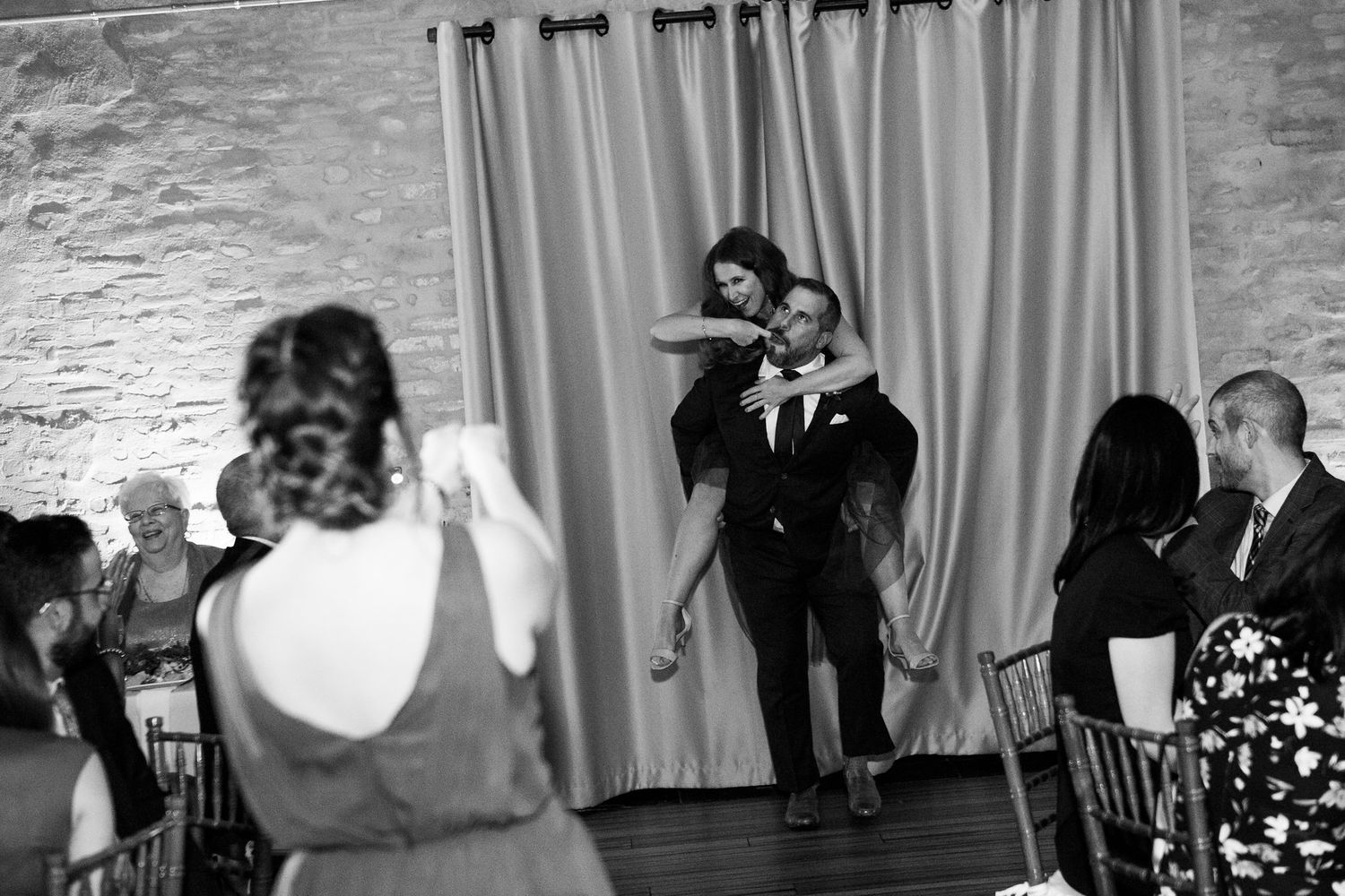 Black and white photo of a groom lifting a guest on the wedding reception dance floor.