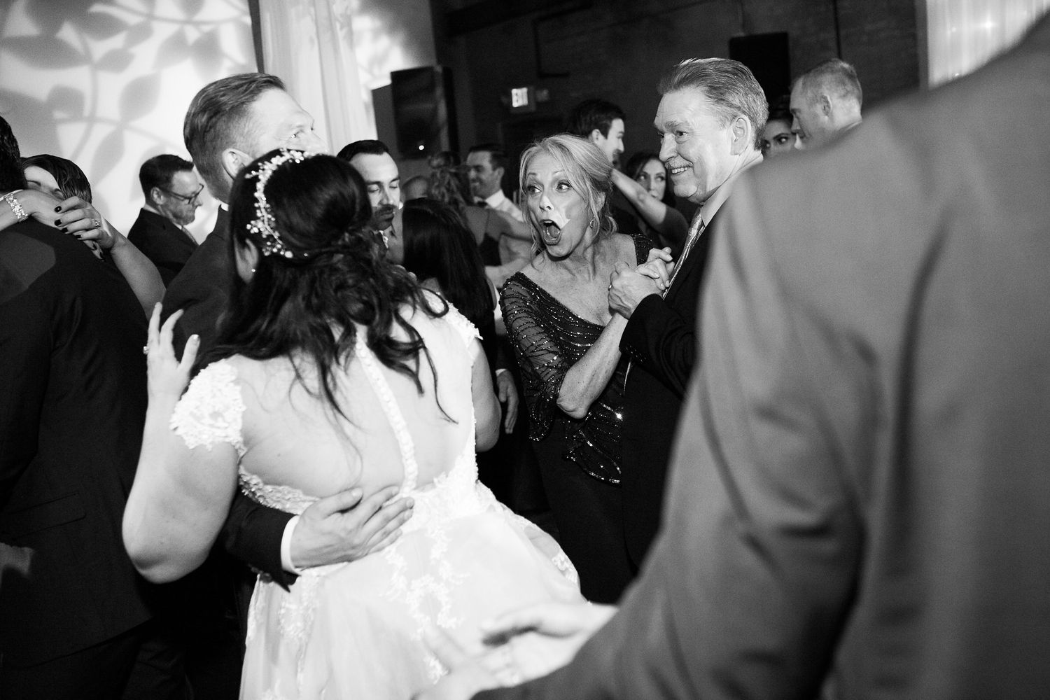 Black and white candid photo of bride dancing with guests at lively wedding reception.
