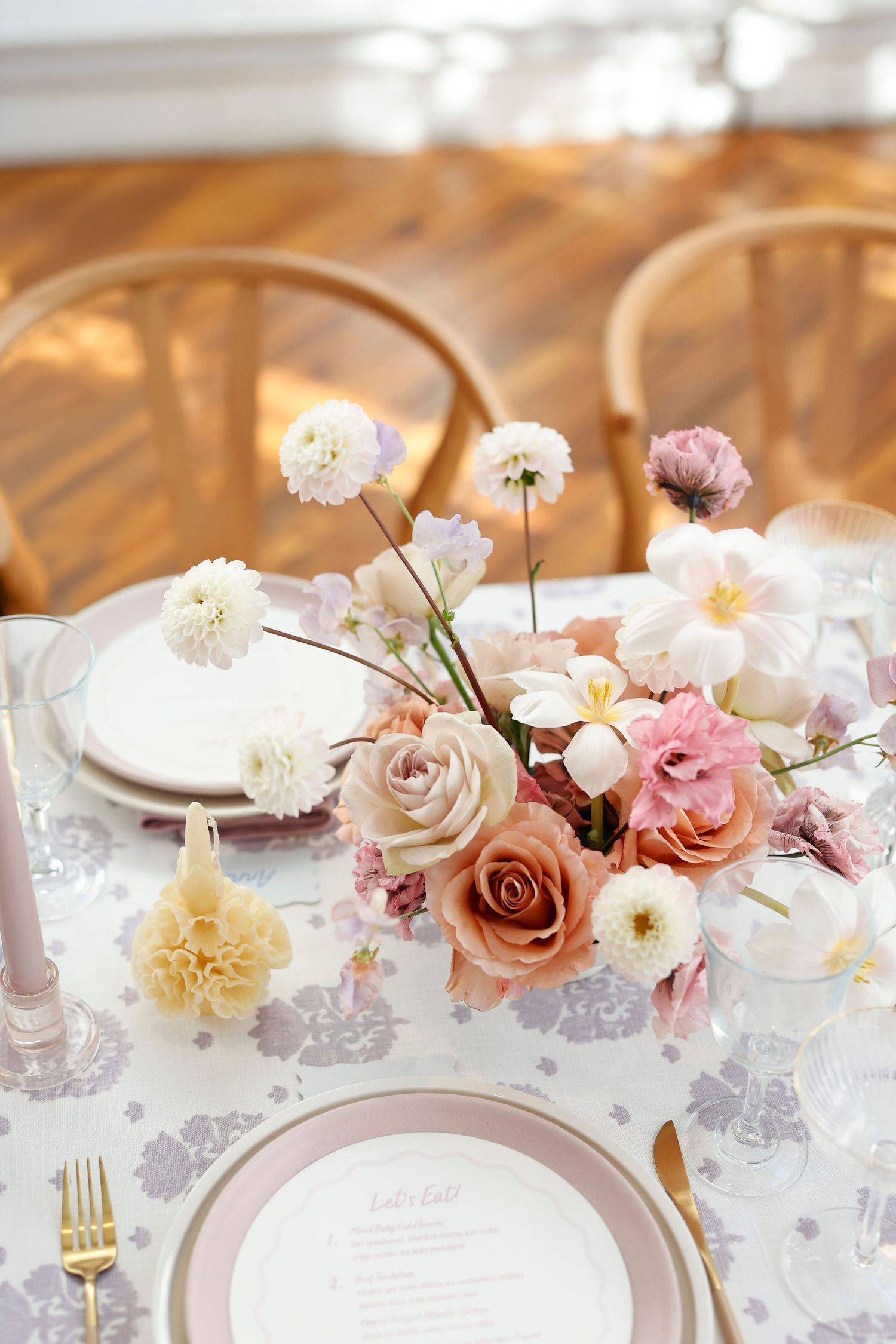 Romantic wedding reception table with soft pink and white floral arrangement, pink candles, and gold cutlery.