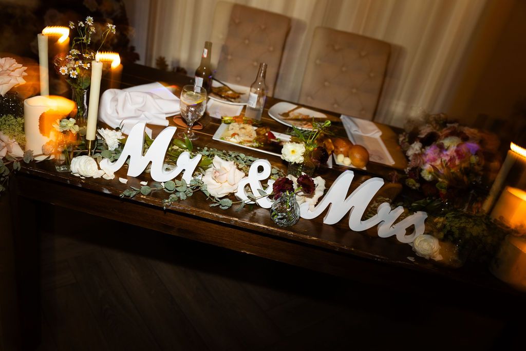 Elegant Mr. and Mrs. sweetheart table decorated with floral arrangements, candles, and greenery at a wedding.