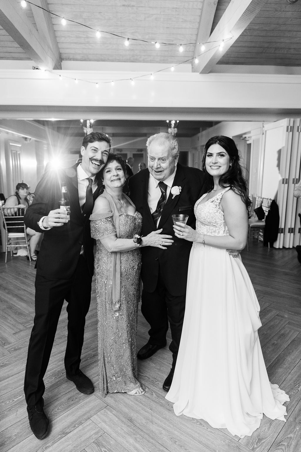 Black and white photo of bride, groom, and grandparents posing together at wedding reception.
