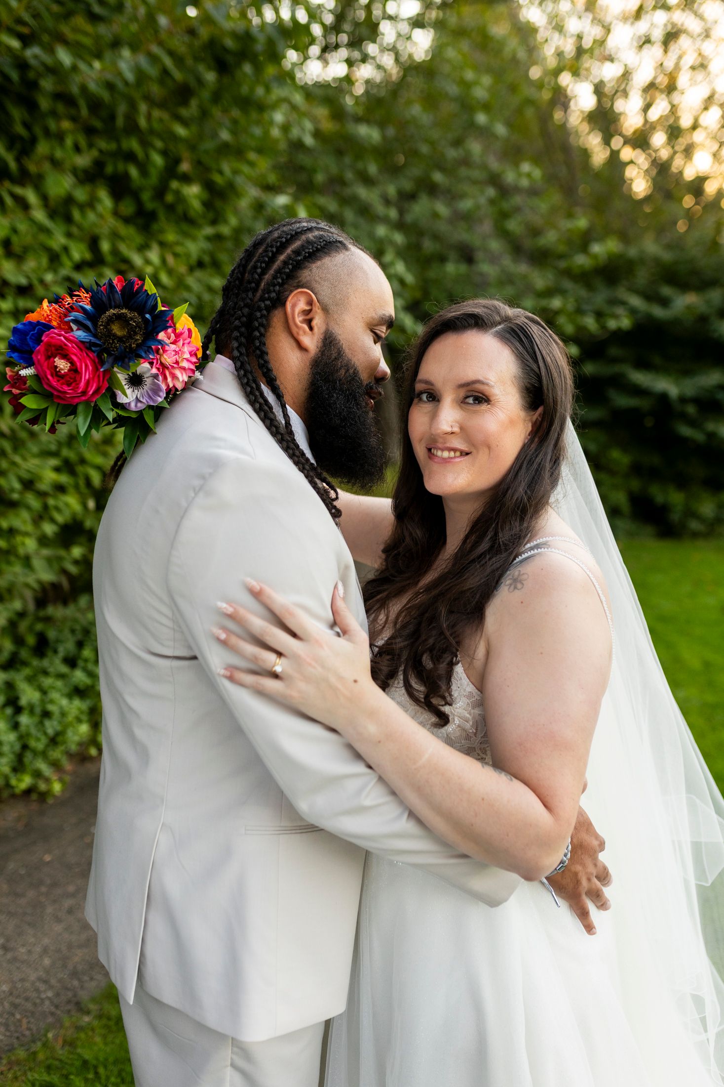 Bride and groom embracing in a lush garden, bride holding a vibrant colorful bouquet.