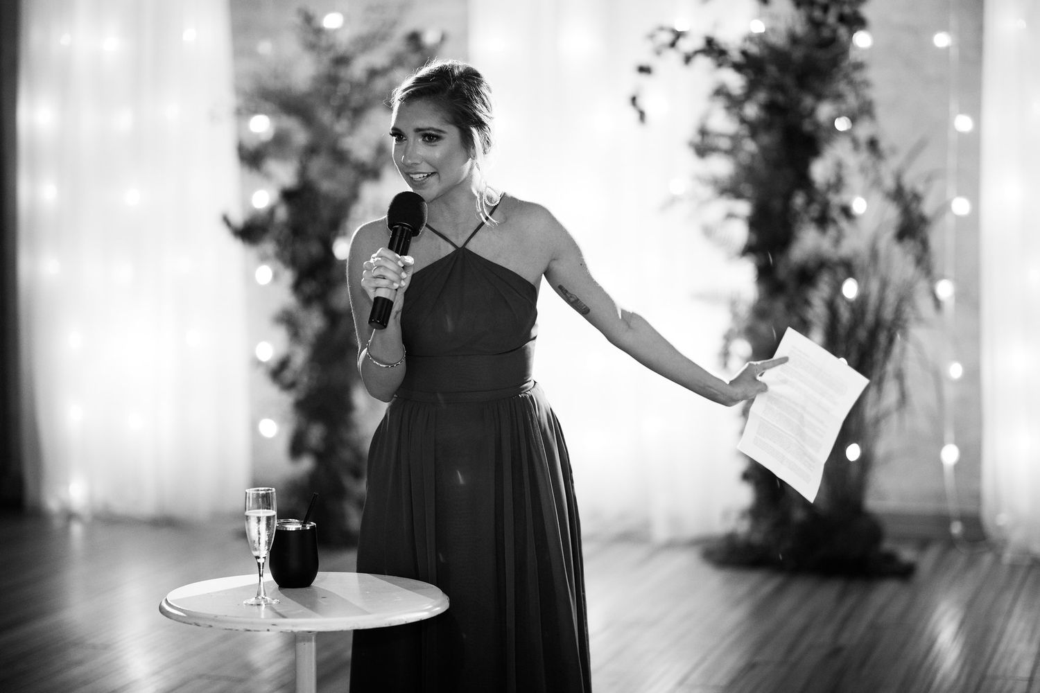 Woman in black gown giving a speech at wedding reception.