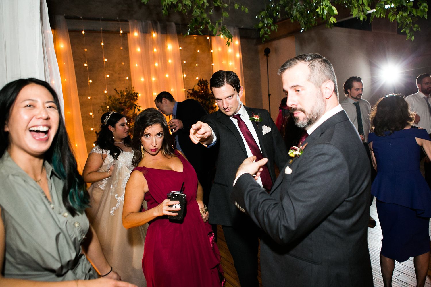 Wedding guests dancing and laughing together at an elegant indoor reception venue.