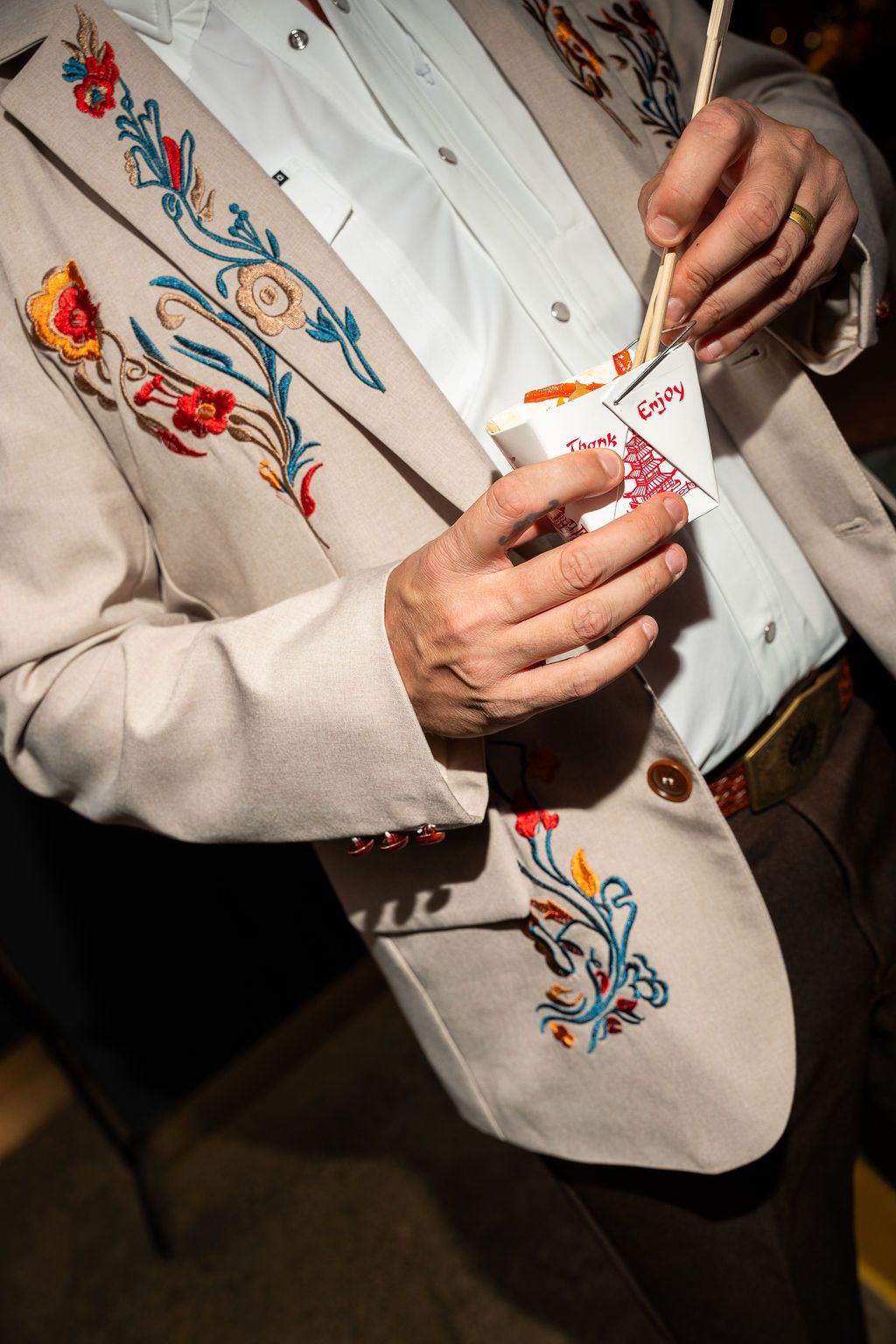 Close-up of hands holding a name tag on an embroidered floral jacket at an event.