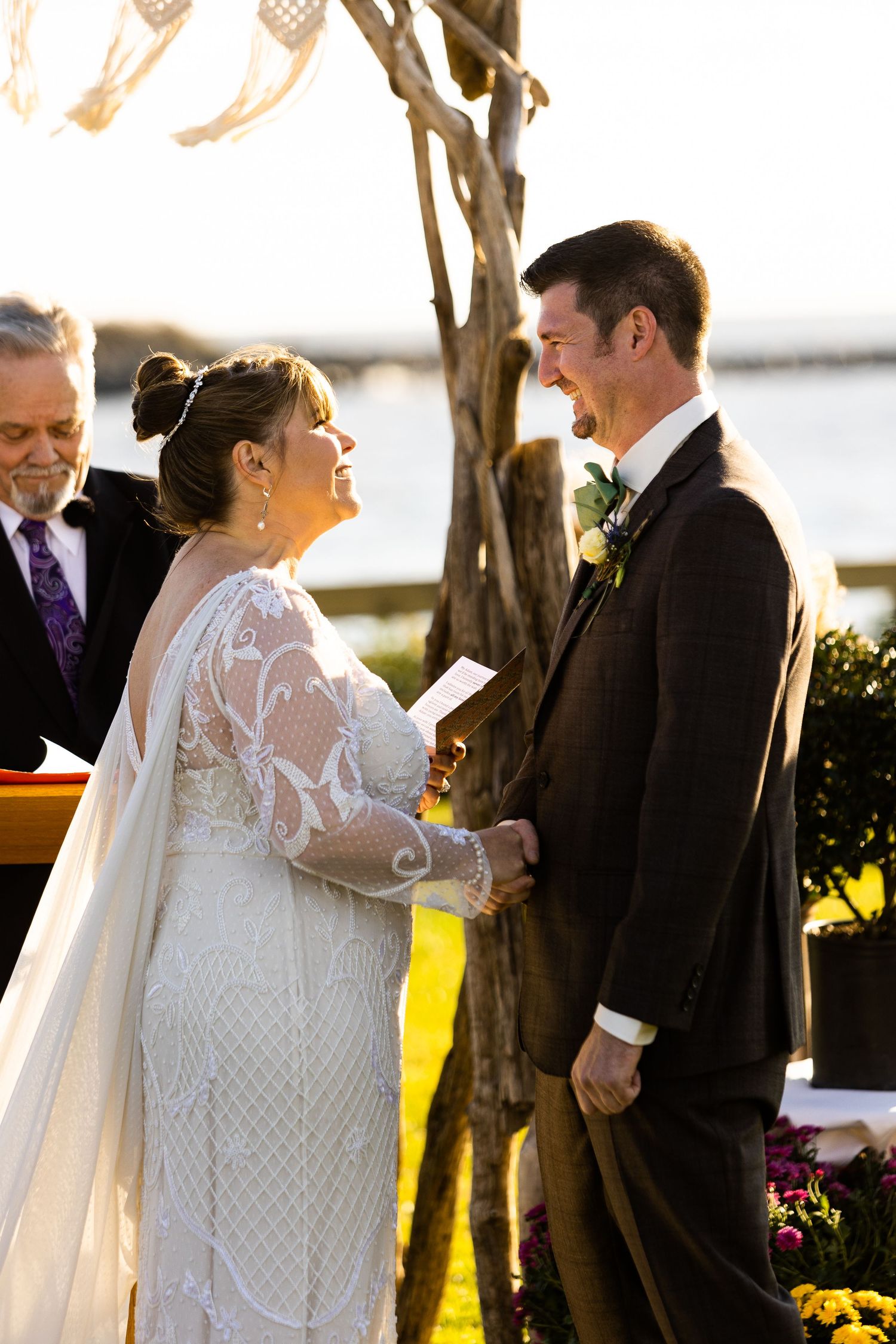 Bride and groom laugh joyfully while exchanging vows at golden hour waterfront wedding.