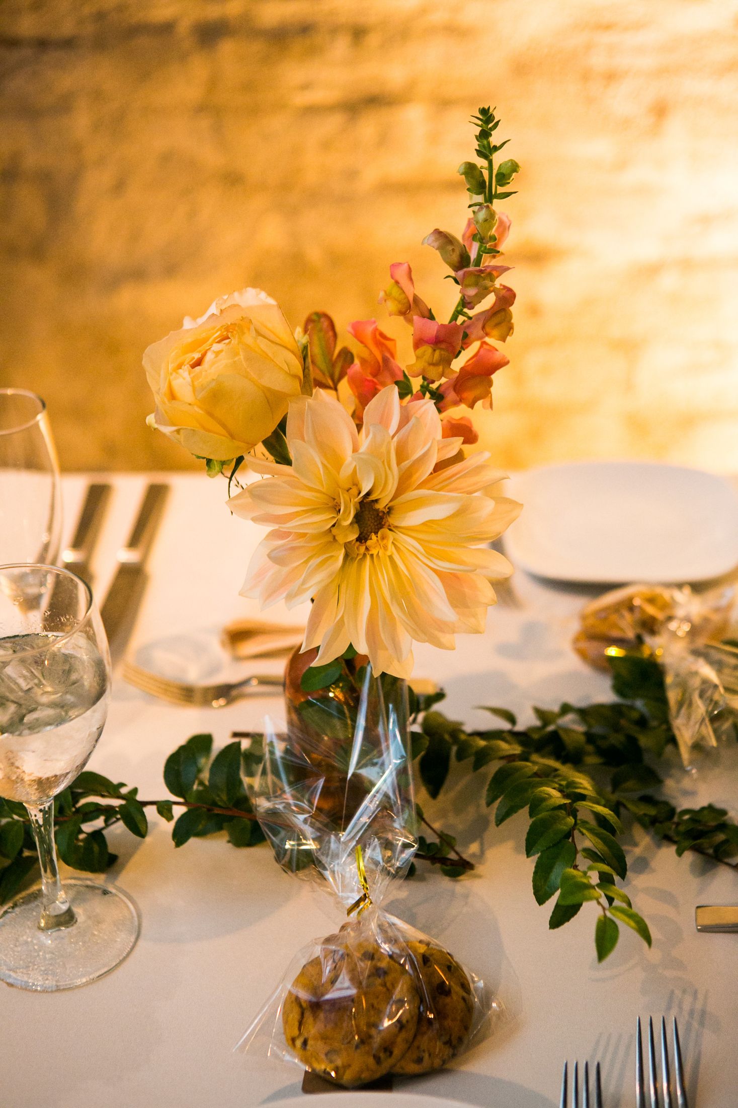 Elegant wedding table centerpiece with yellow dahlia and roses in glass vase with greenery.
