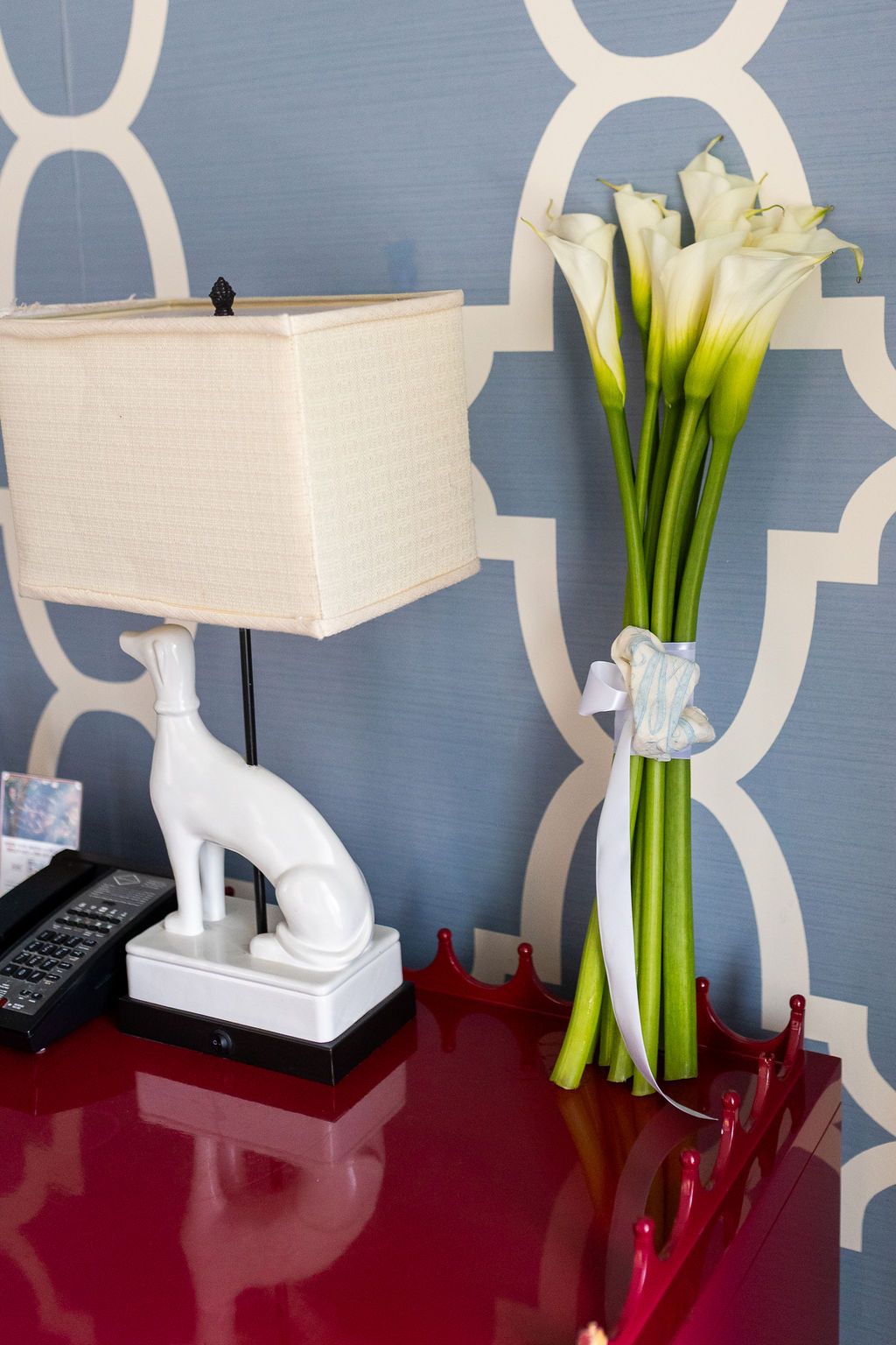 White calla lily bridal bouquet tied with ribbon beside a lamp with a greyhound figurine.