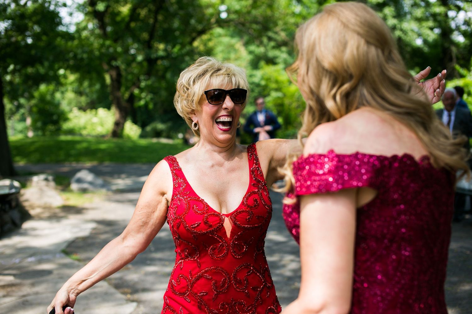 Two women in red dresses laughing together outdoors at a wedding celebration.