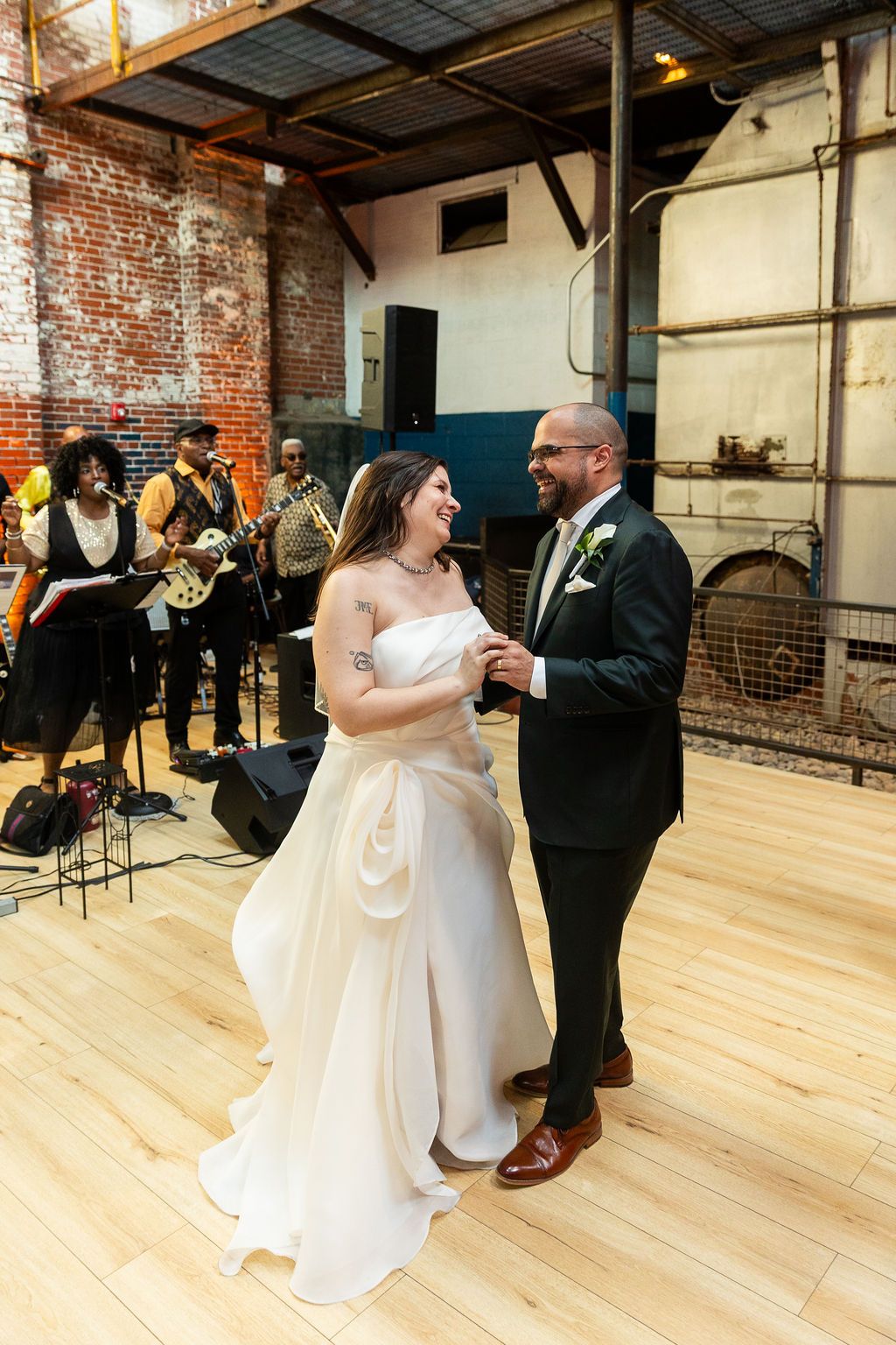 Smiling bride and groom dance together at wedding reception with live band performing in the background.