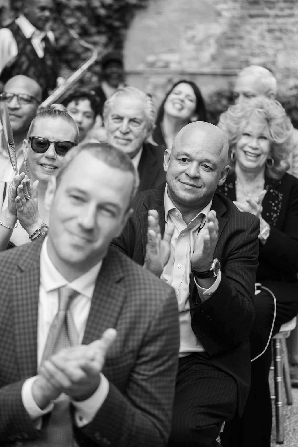 Black and white photo of wedding guests clapping and smiling during an outdoor ceremony.