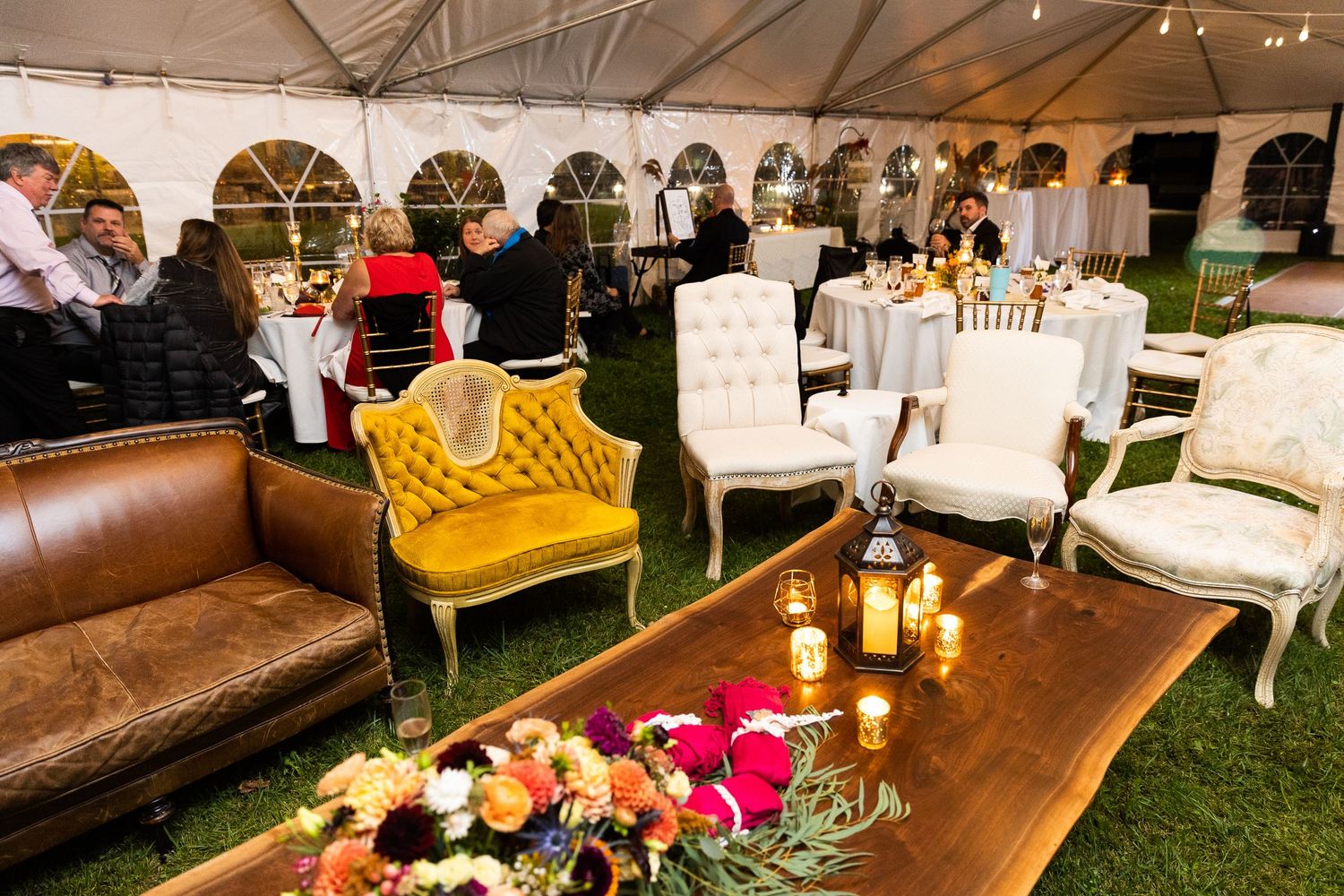 Elegant wedding reception tent with vintage lounge furniture, candles, and colorful floral arrangements.