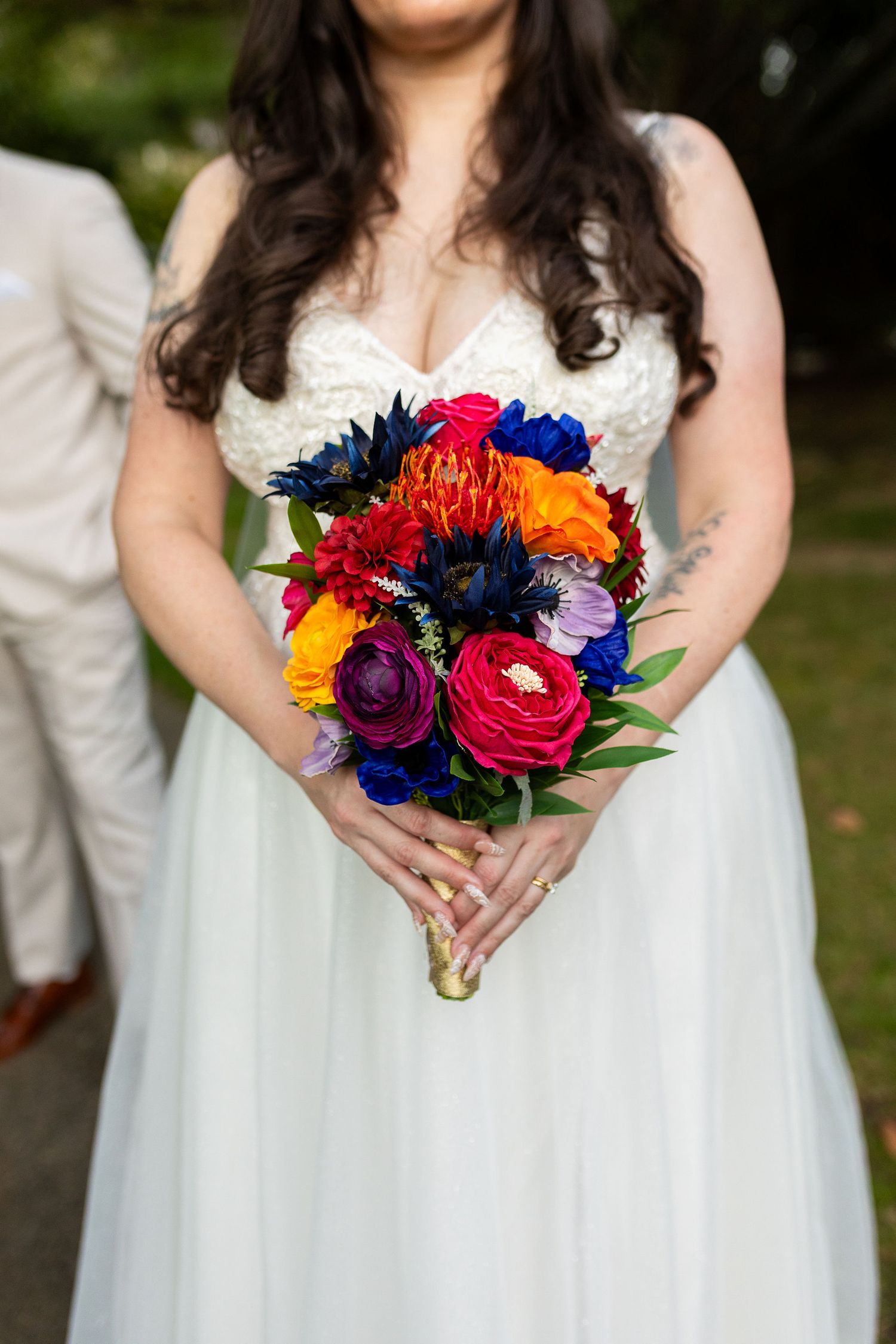 Bride in white gown holding vibrant colorful wedding bouquet with red, orange, blue, and purple flowers.