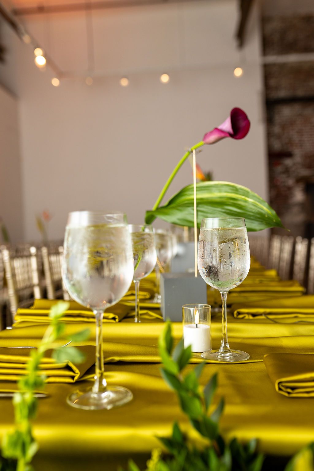 Elegant wedding table setting with yellow linens, water glasses, candles, and a purple calla lily.