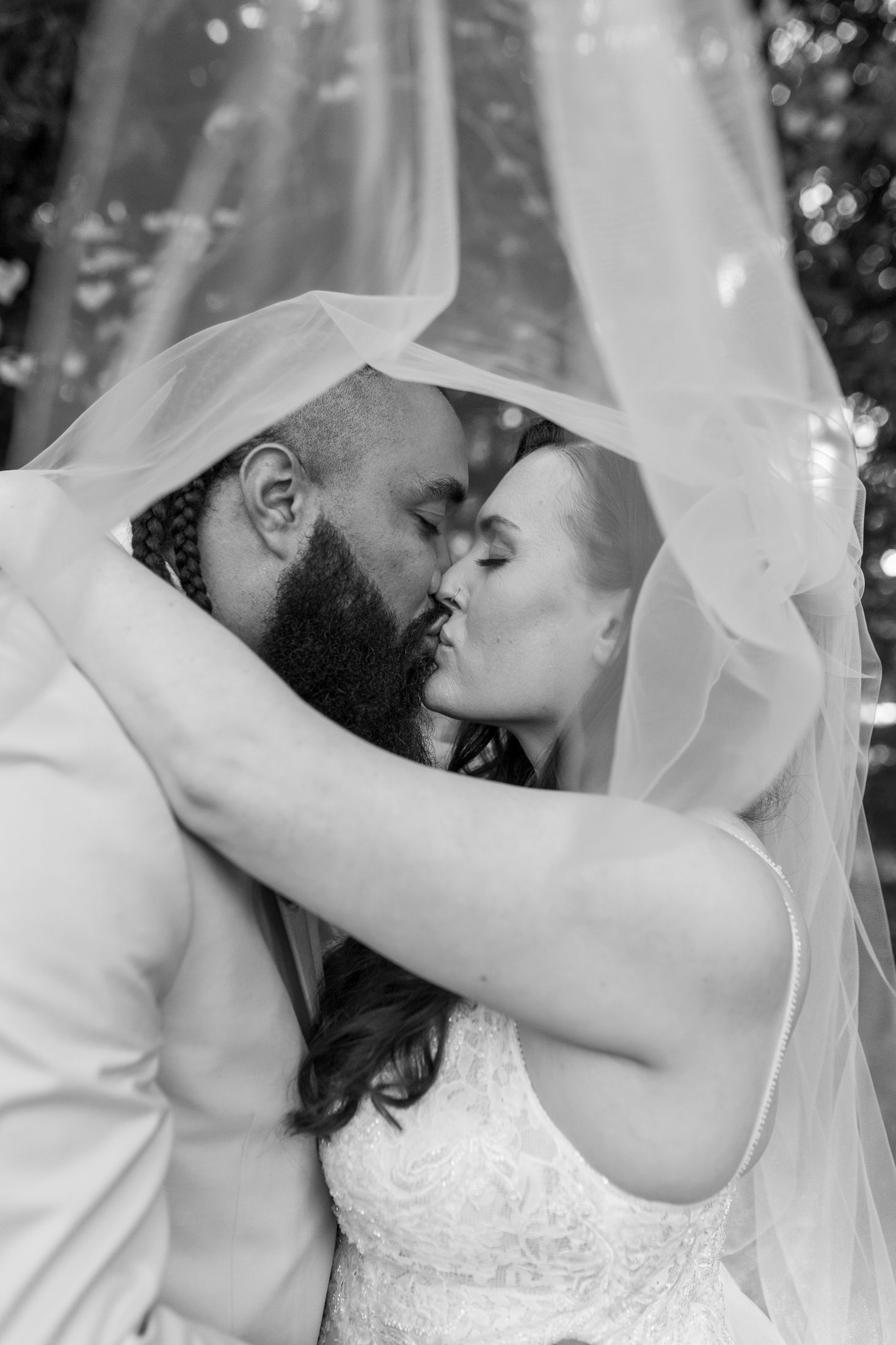Black and white photo of bride and groom kissing under wedding veil.