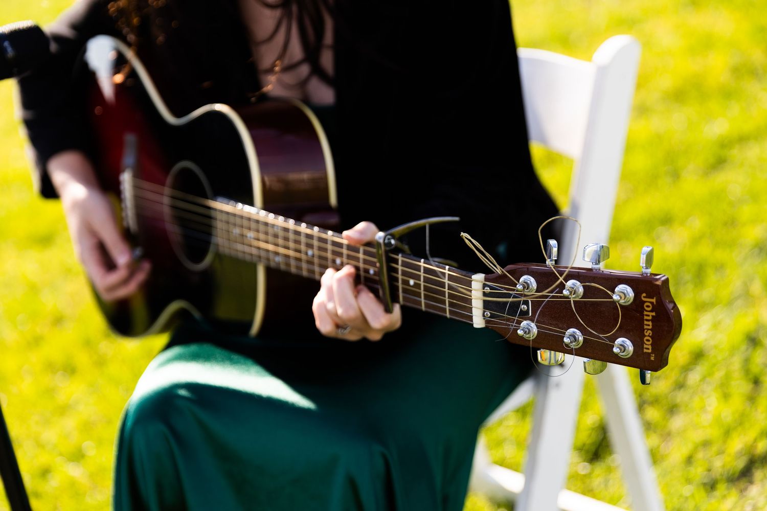 Close-up of musician playing acoustic guitar at outdoor wedding ceremony on green grass.