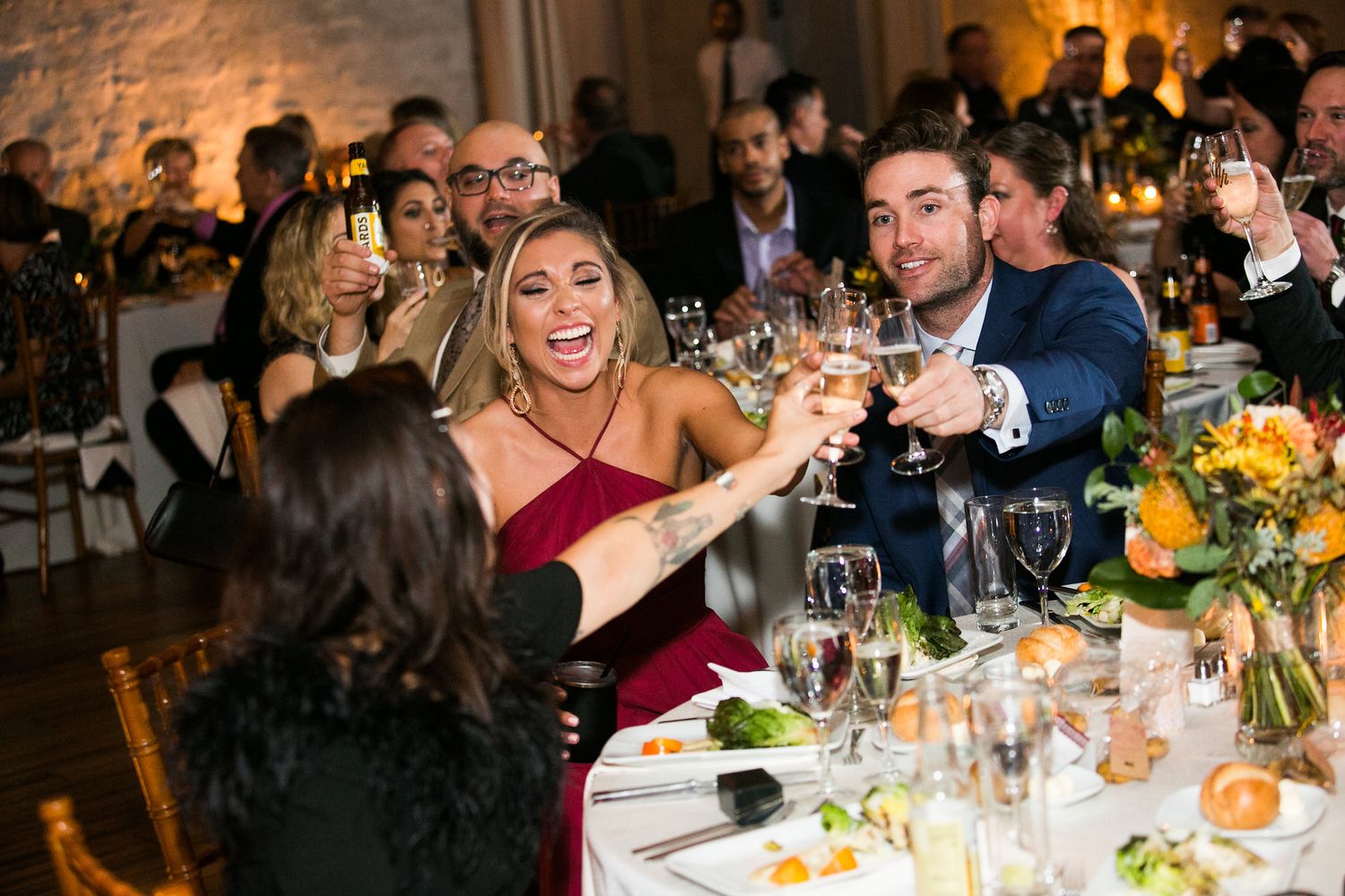 Wedding guests in formal wear toast with champagne glasses at an elegant reception dinner.
