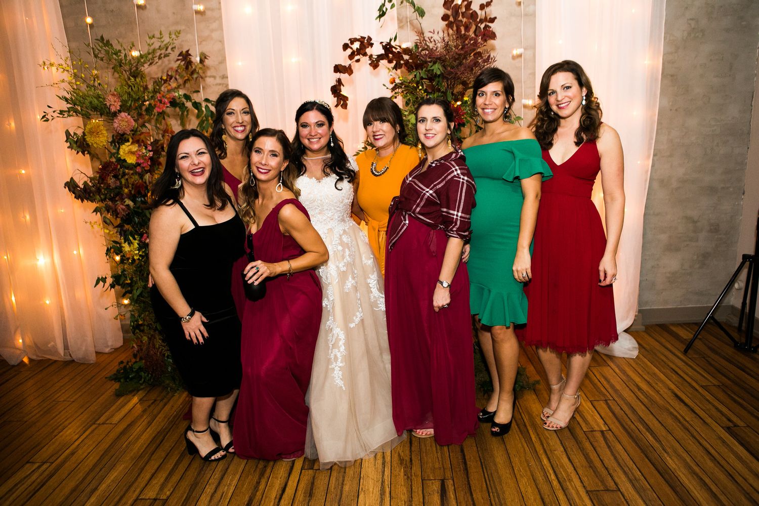 Bride posing with seven female guests in colorful dresses at wedding reception.