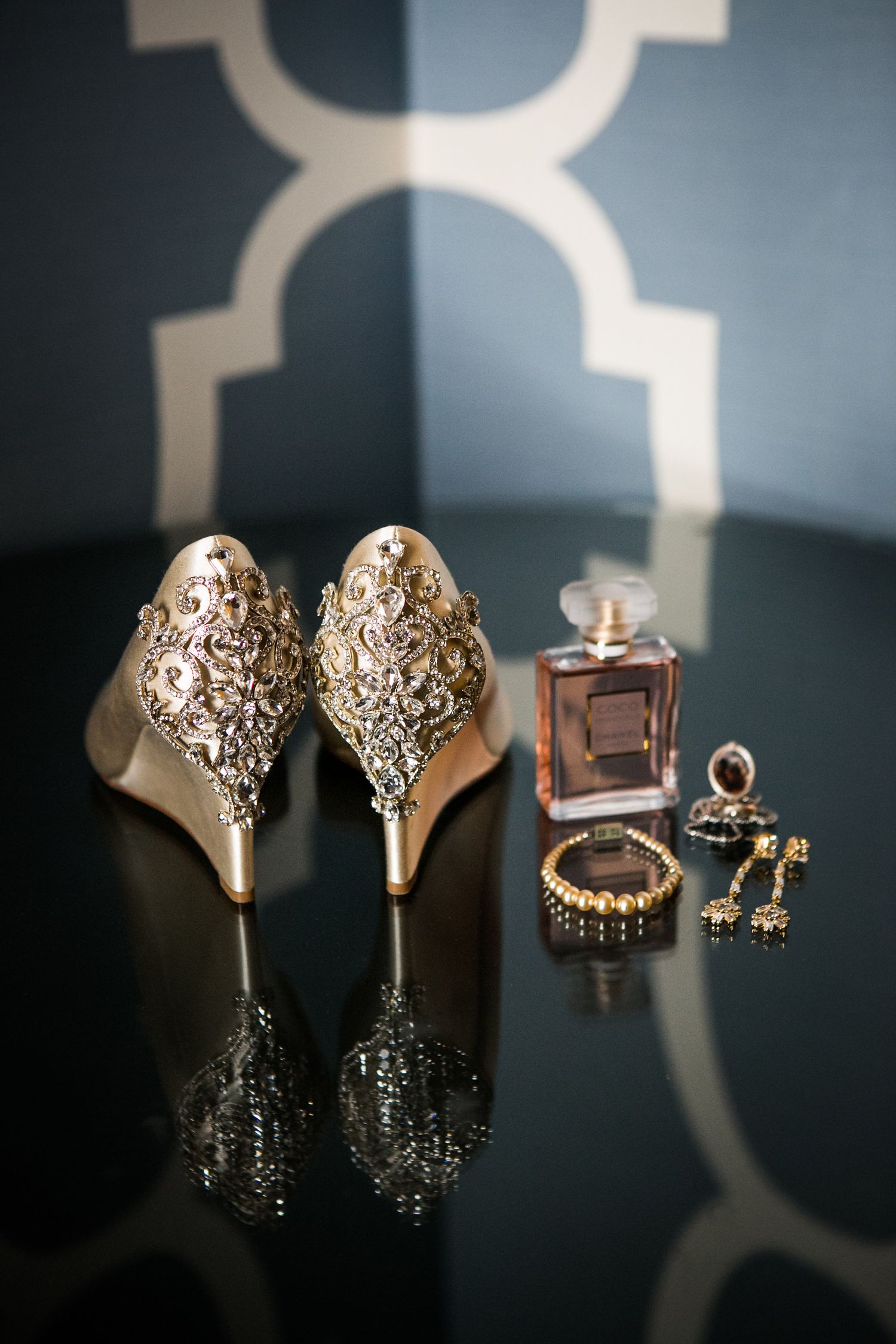 Ornate gold bridal heels with Chanel perfume, pearl bracelet, and drop earrings on dark surface.