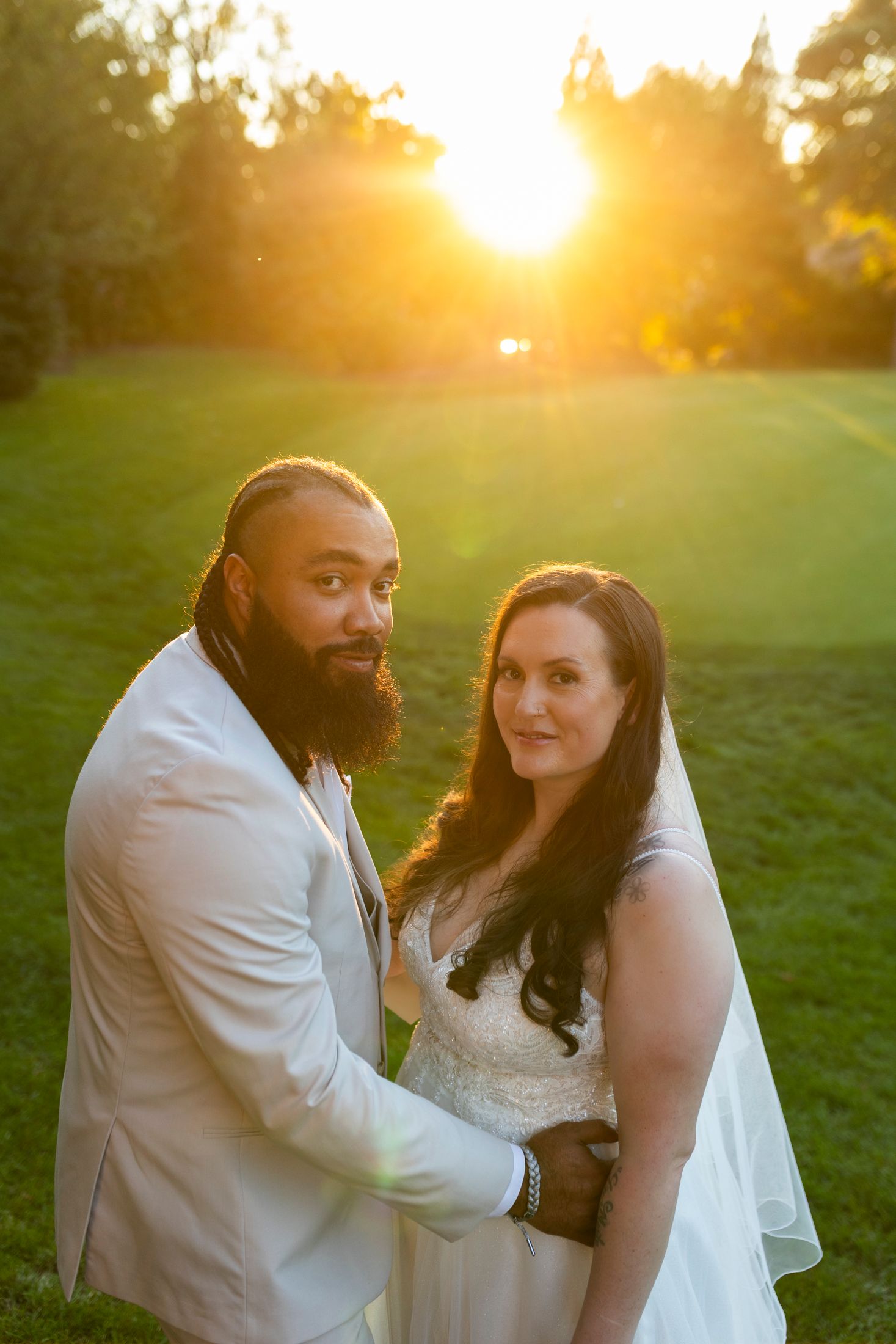 Bride and groom portrait with stunning golden sunset glowing behind them on a green lawn.