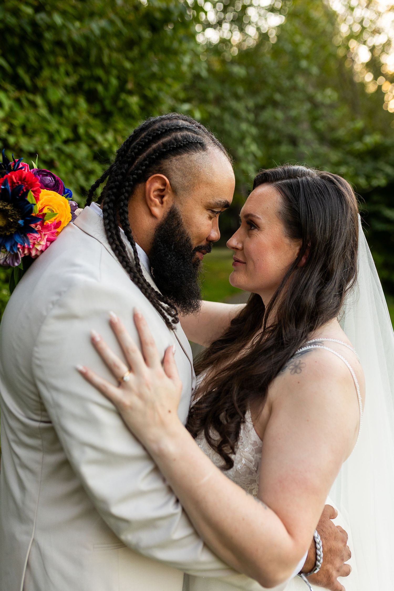 Bride and groom with braided hair and colorful floral accessory share an intimate forehead touch outdoors.