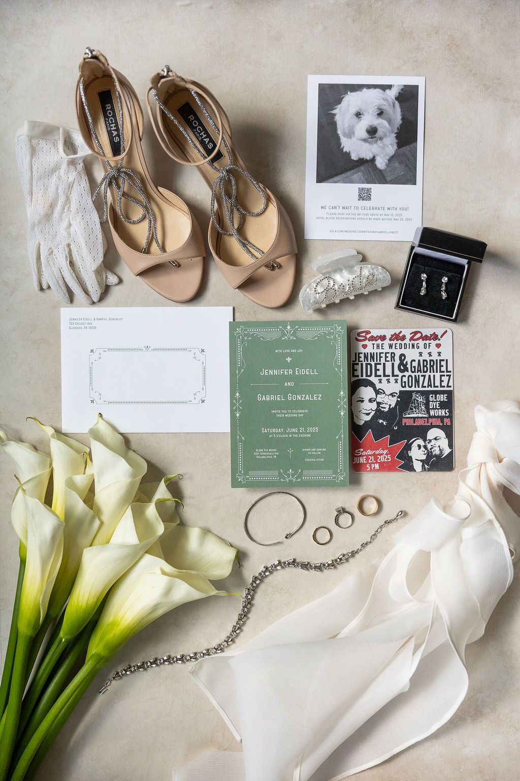 Wedding flat lay featuring green invitation suite, nude heels, calla lilies, jewelry, and save the date for Jennifer and Gabriel.