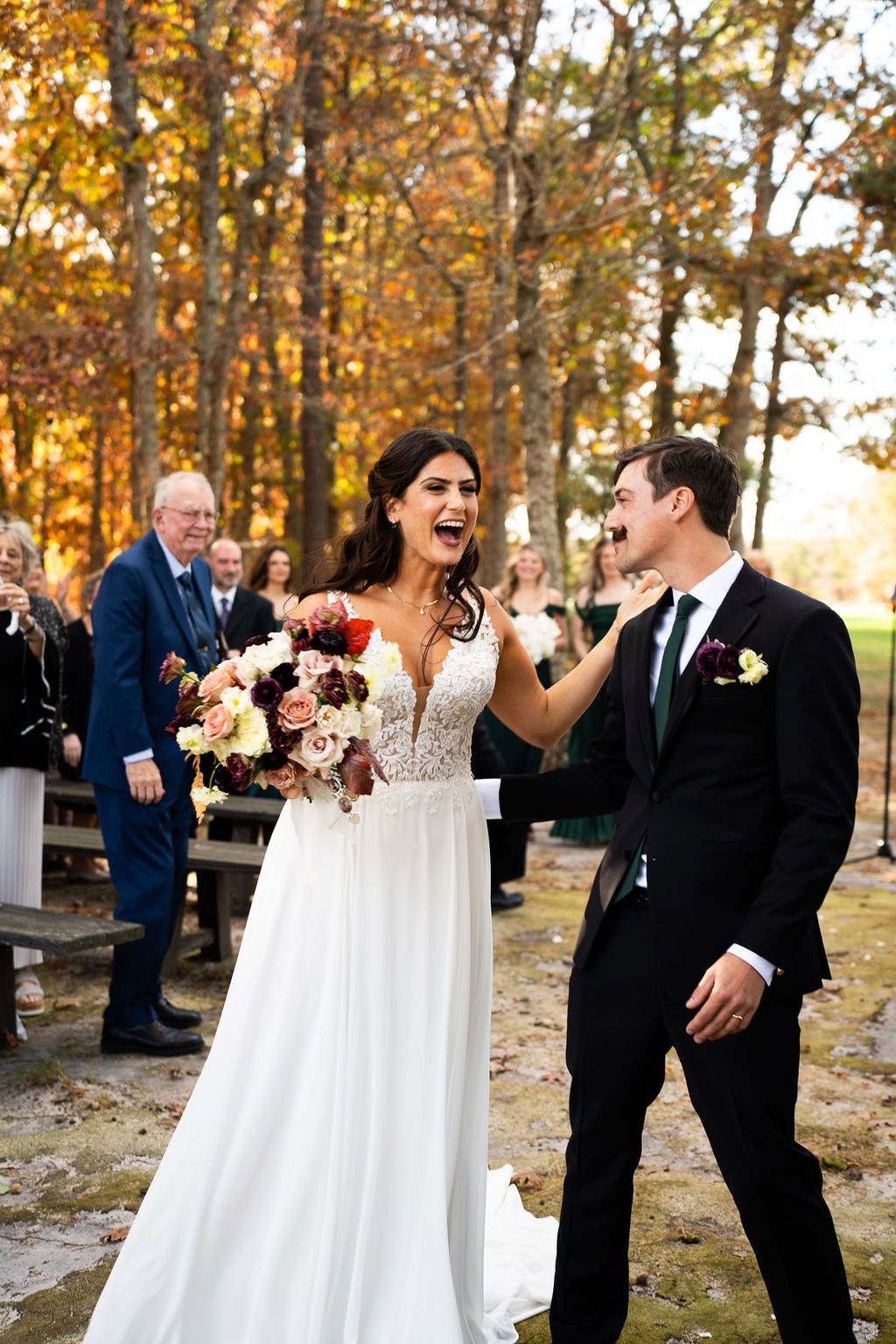 Joyful bride laughs with groom after outdoor fall wedding ceremony surrounded by colorful autumn trees.
