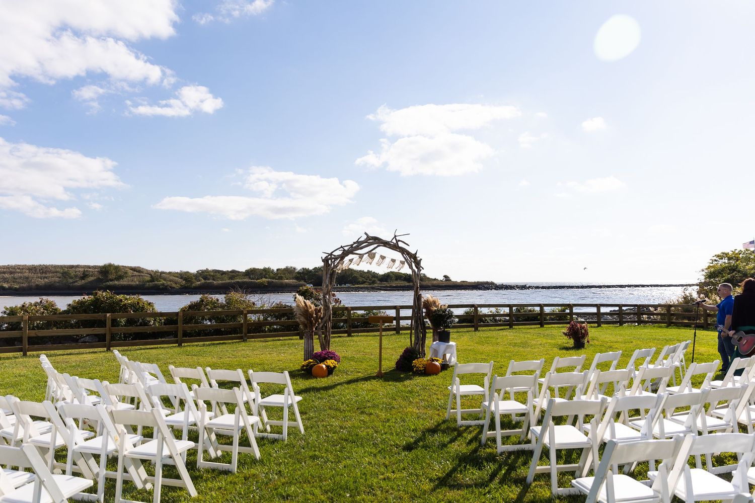 Outdoor wedding ceremony setup with white chairs, floral arch, and scenic waterfront backdrop.