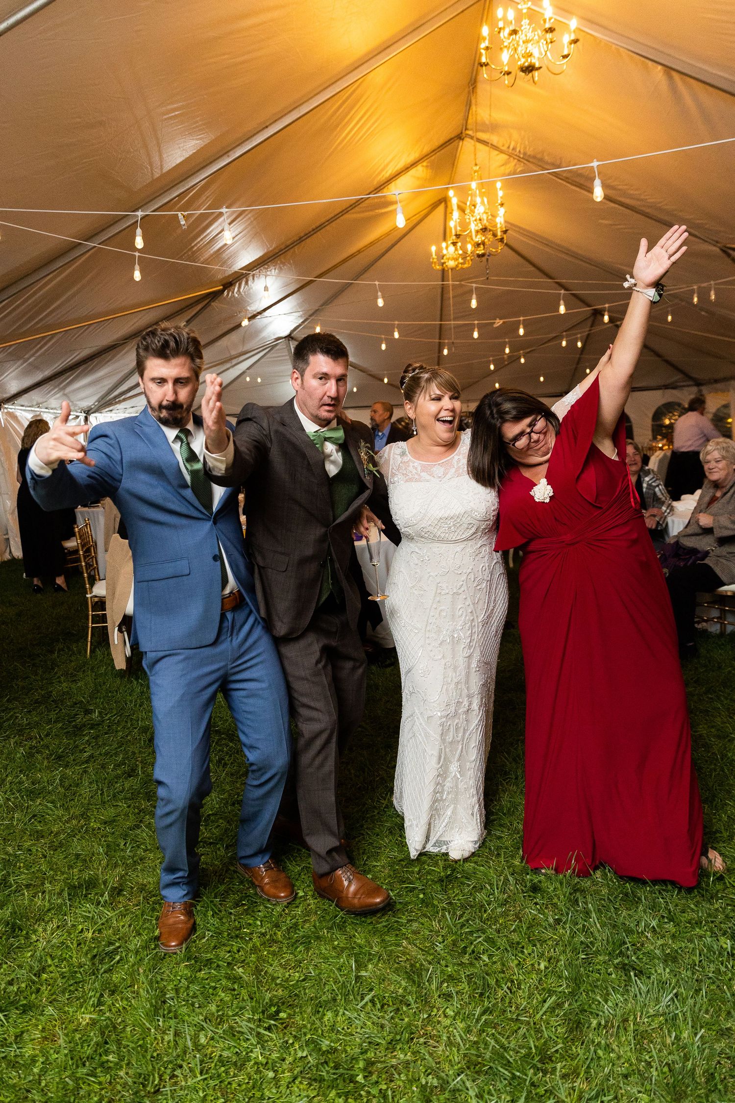 Colorful wedding party photo with bride in white and guests celebrating under a festive tent.