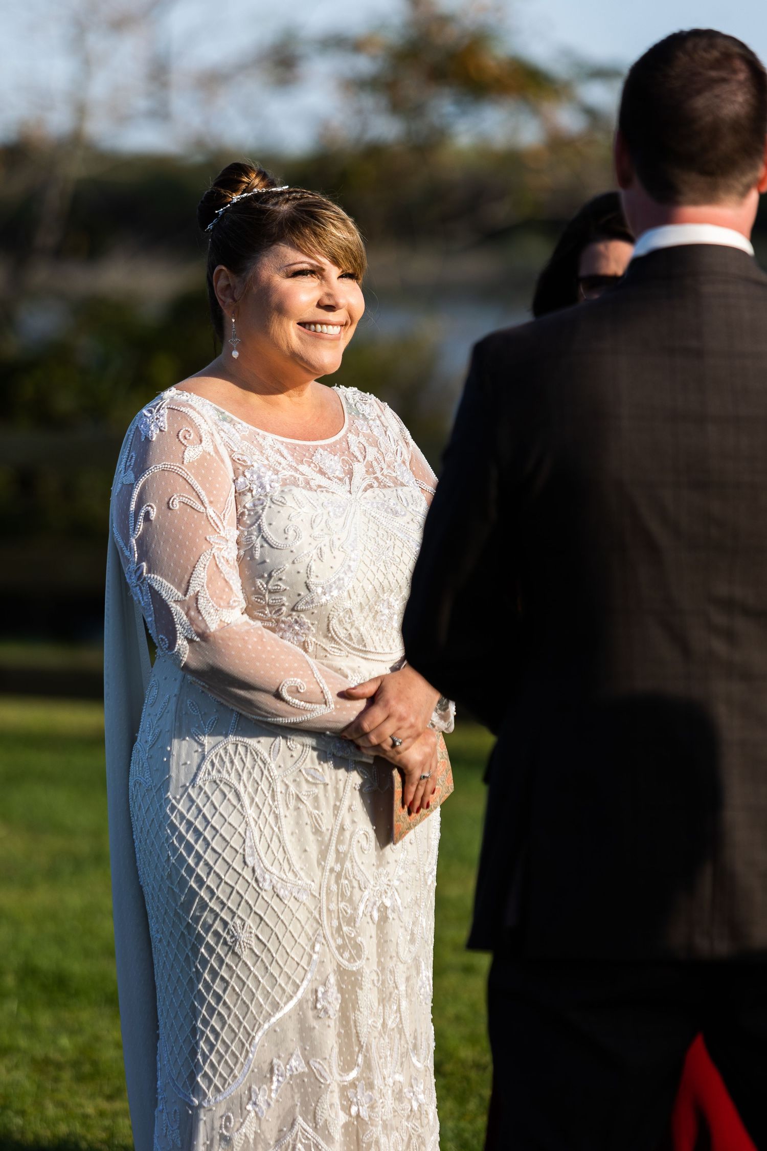 Bride in beaded lace gown smiling joyfully at groom during outdoor fall wedding ceremony.