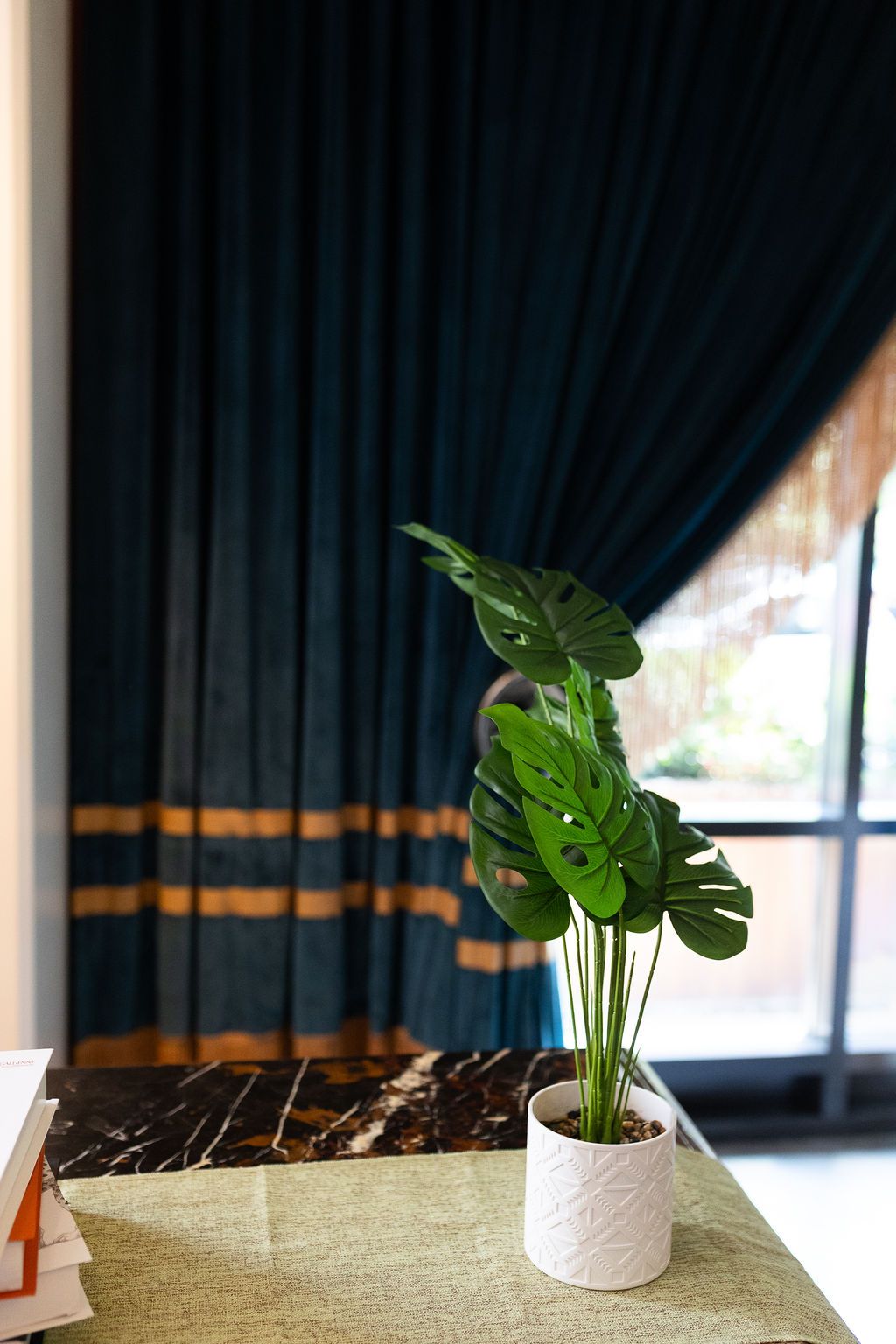 Monstera plant in white pot on marble table with teal velvet curtains at Hotel Monaco wedding venue.