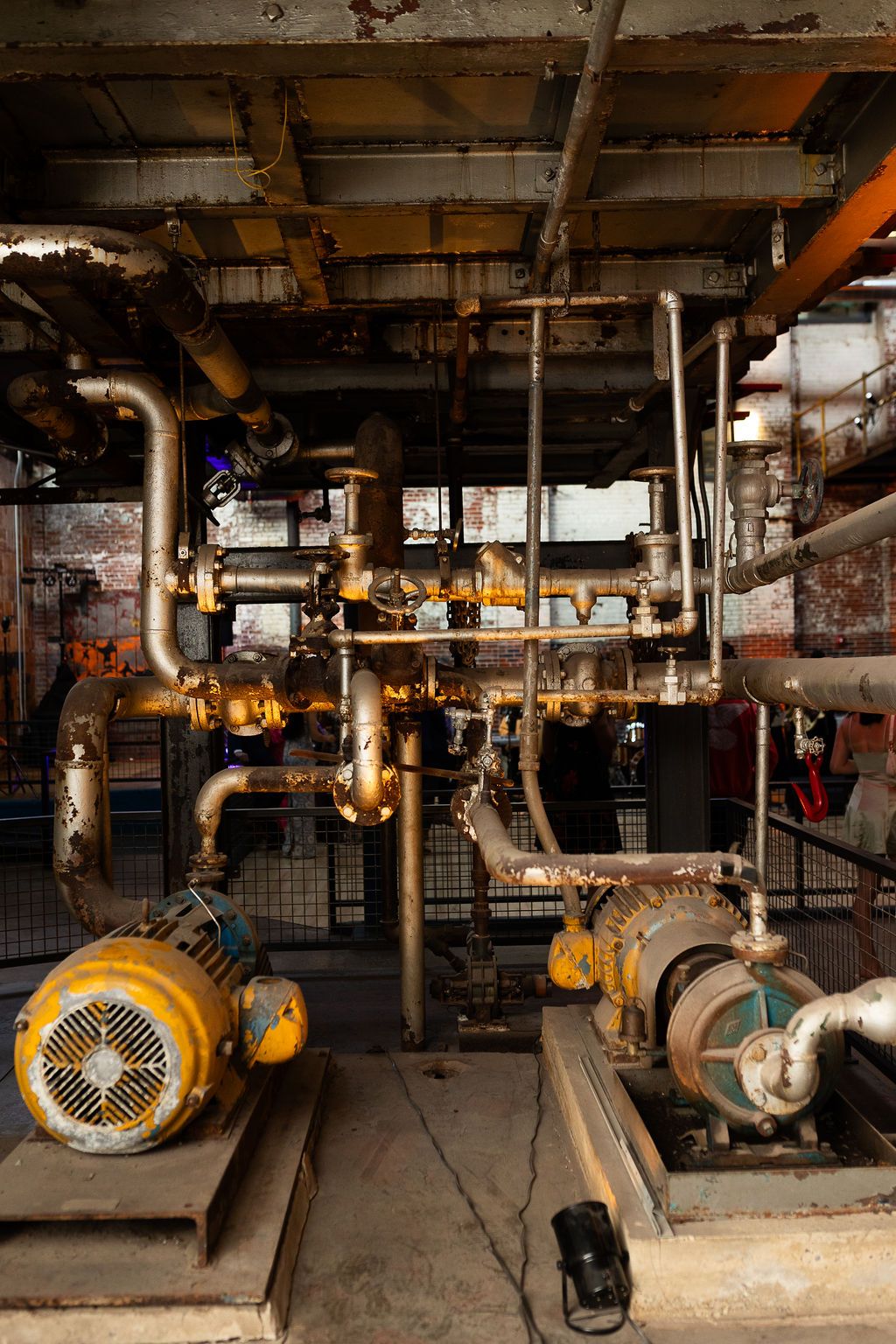Vintage industrial machinery with yellow motors and rusty pipes in an old factory building.