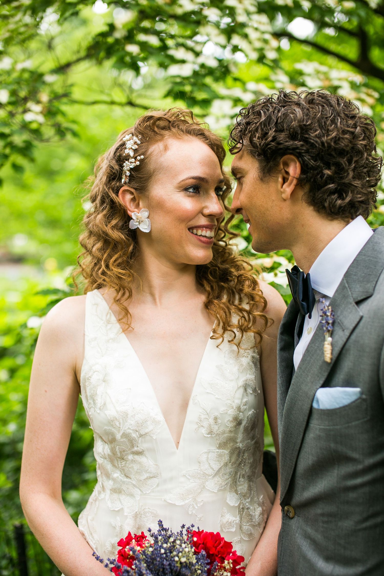 Close-up of radiant bride smiling as groom leans in close, both surrounded by lush green garden backdrop.