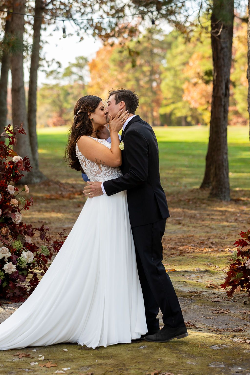 Bride and groom share first kiss as newlyweds at outdoor fall wedding ceremony among autumn trees.