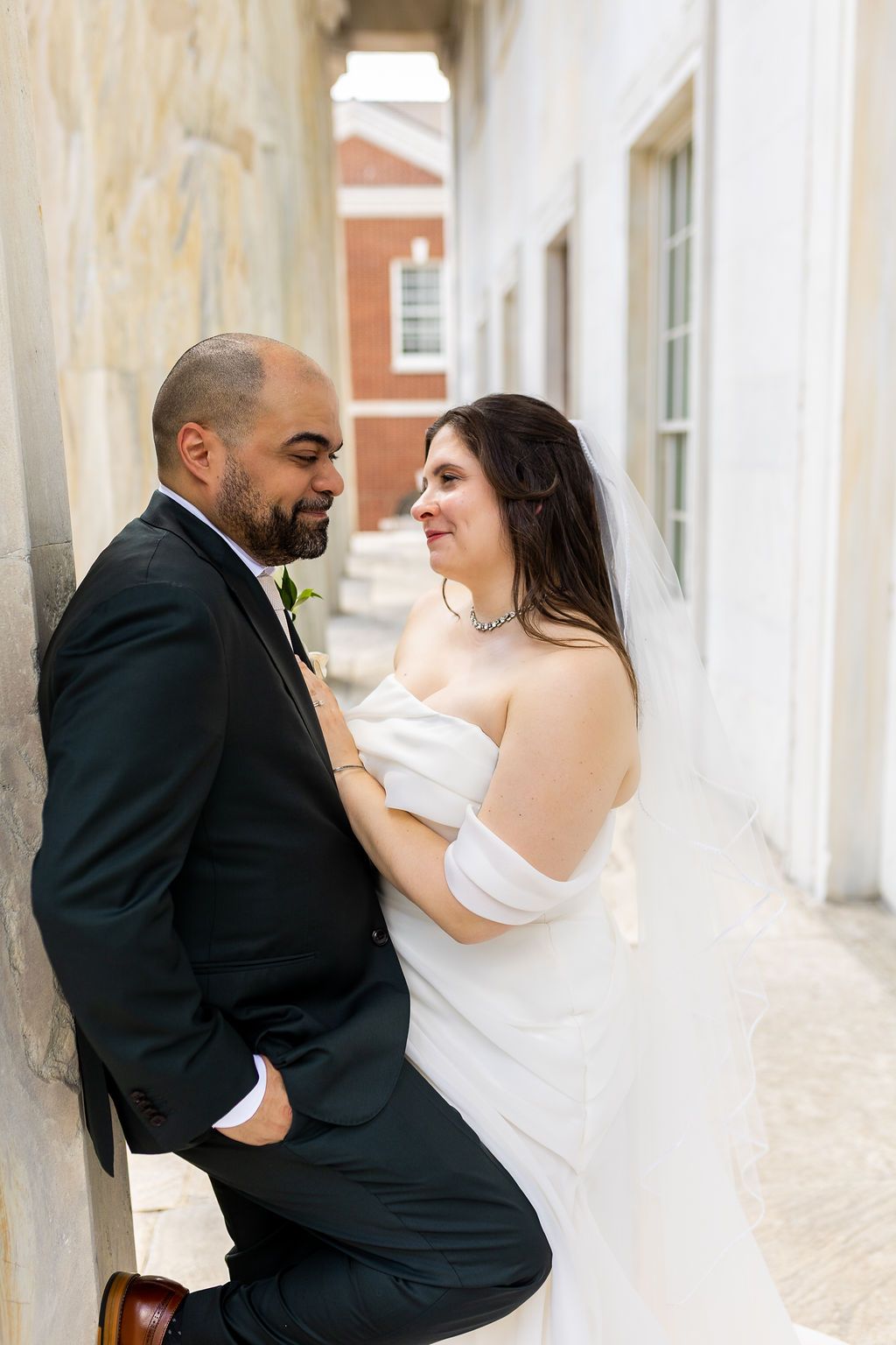 Bride and groom sharing an intimate moment leaning against a stone wall at their wedding.