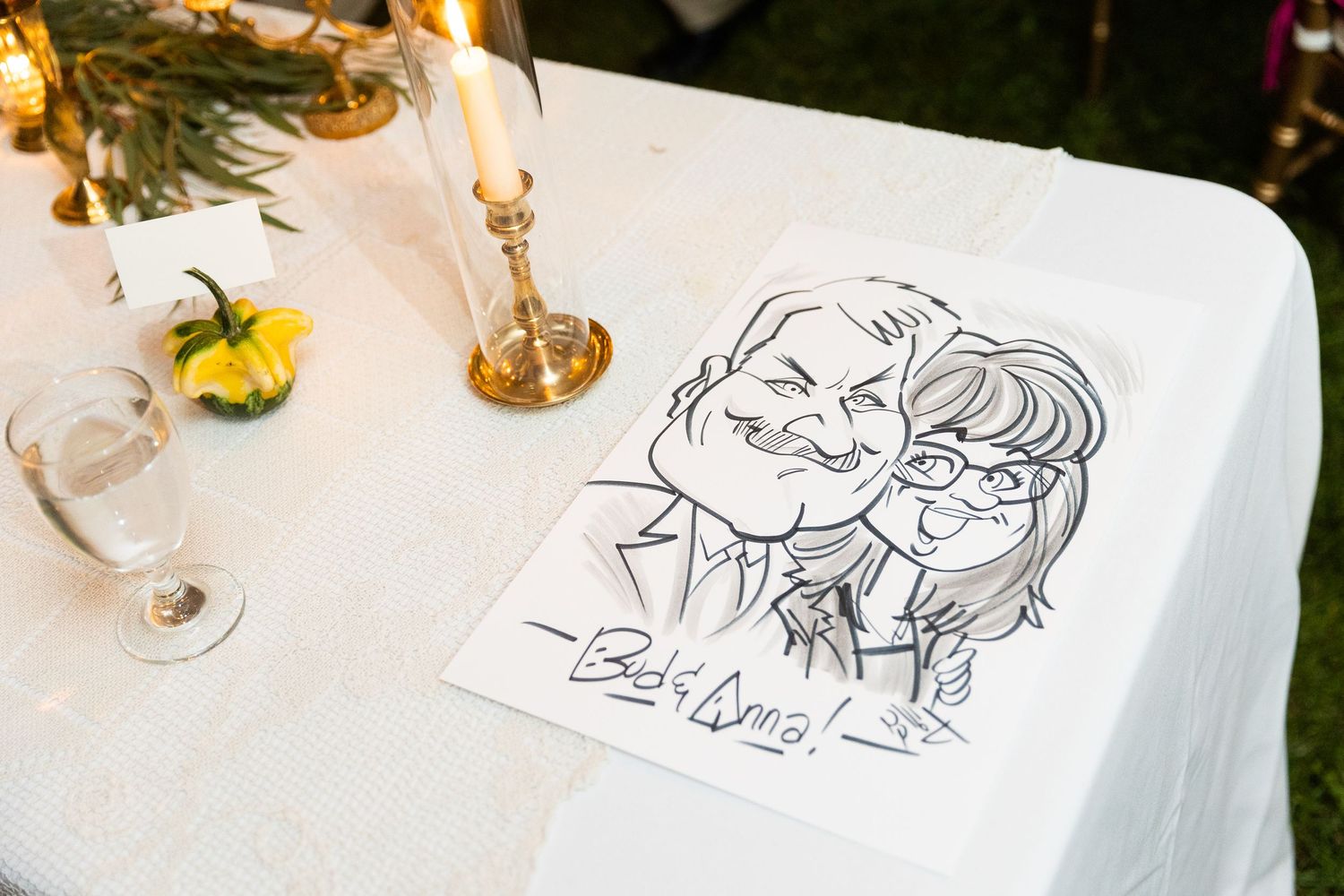 Hand-drawn caricature of couple signed Bob and Anna displayed on white tablecloth at wedding.