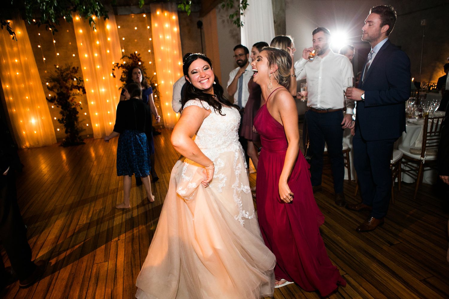 Bride in white gown dancing with a guest in burgundy dress at wedding reception.