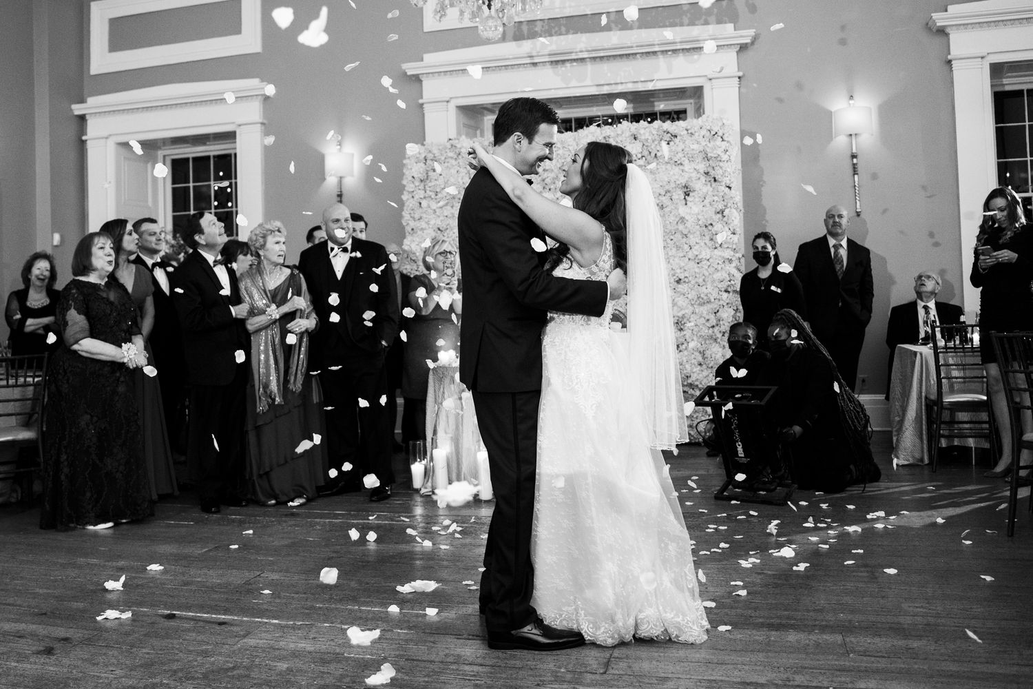 Black and white photo of bride and groom sharing first dance as petals fall around them.