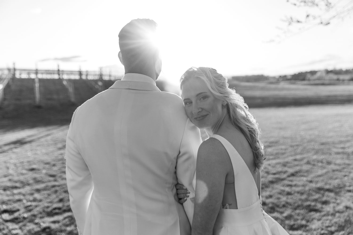 Black and white photo of smiling bride walking with groom at sunset.