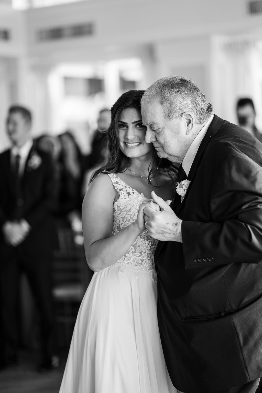 Bride in lace wedding gown shares emotional father-daughter dance, black and white wedding photo.