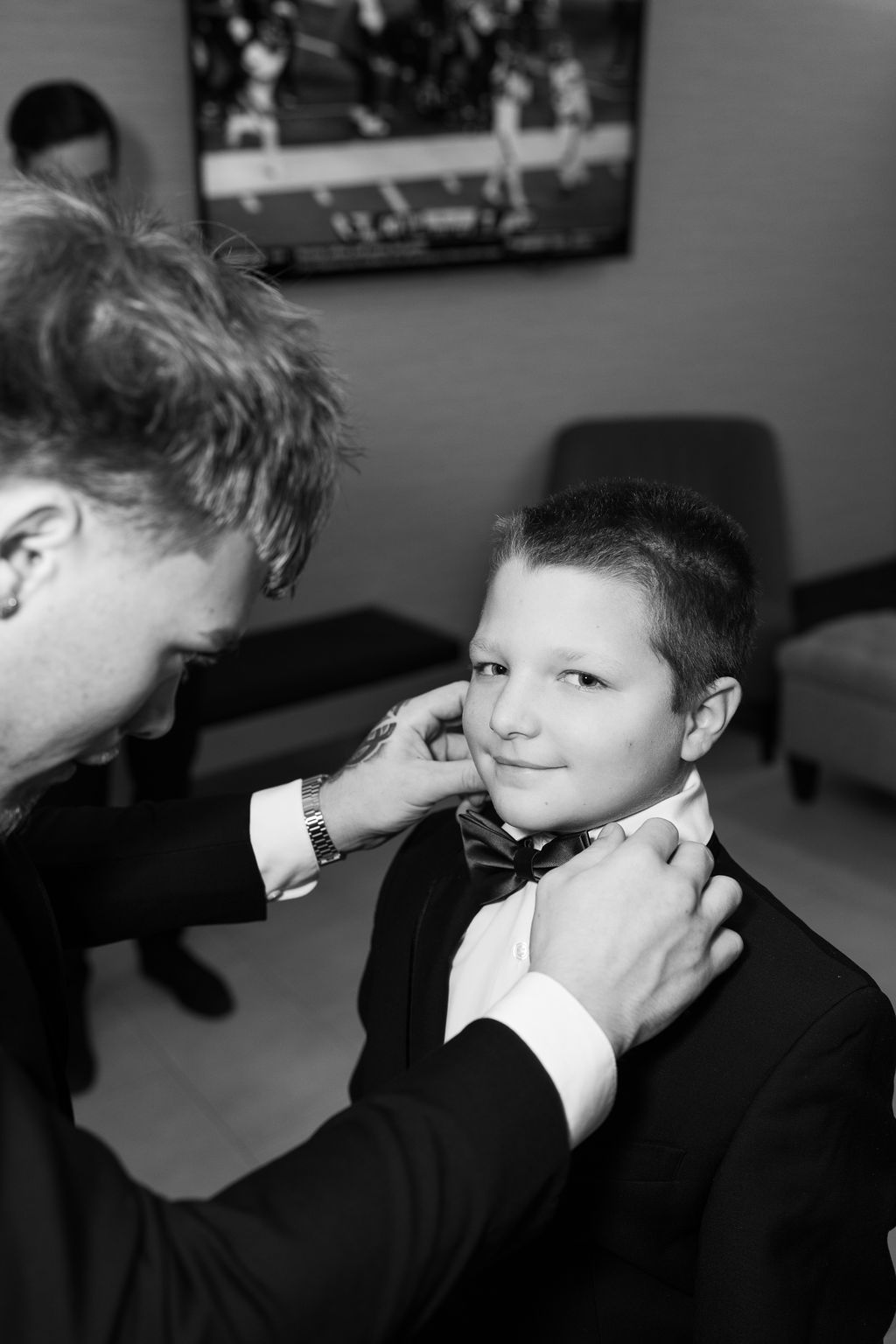 Black and white photo of a man adjusting a young boy's bow tie before a wedding ceremony.