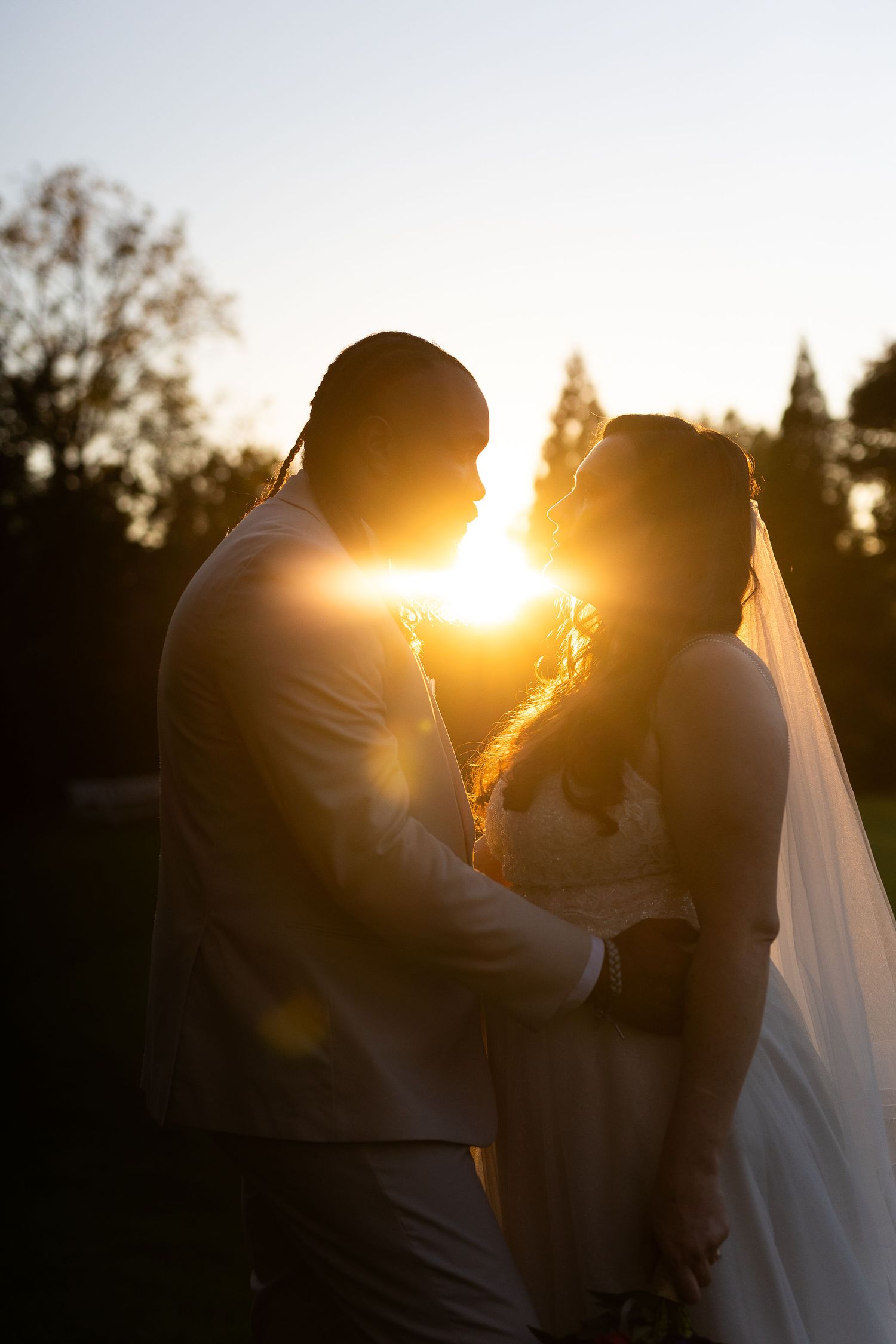 Romantic silhouette of bride and groom facing each other with golden sunset light glowing between them.