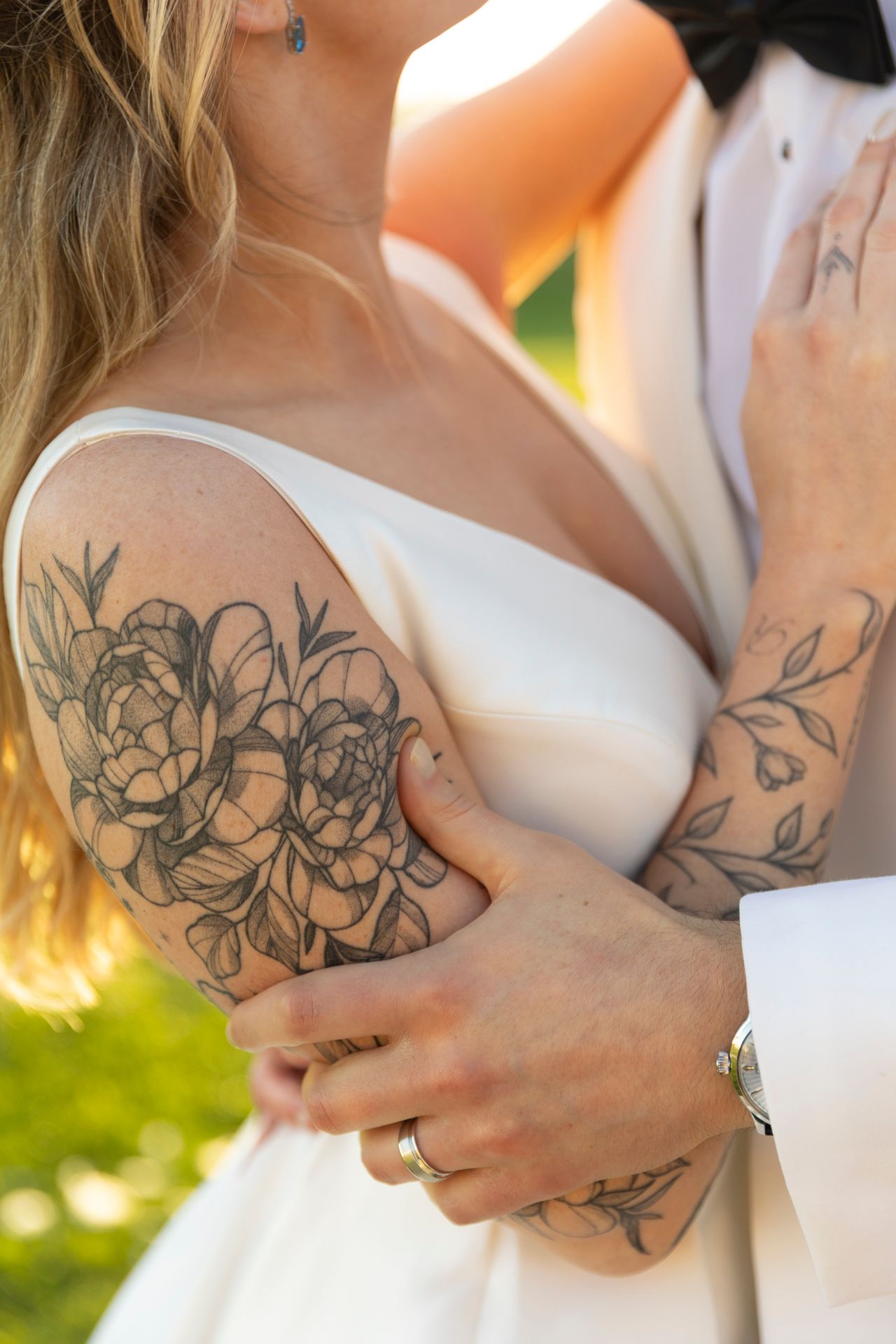 Close-up of bride and groom embracing showing floral arm tattoos.