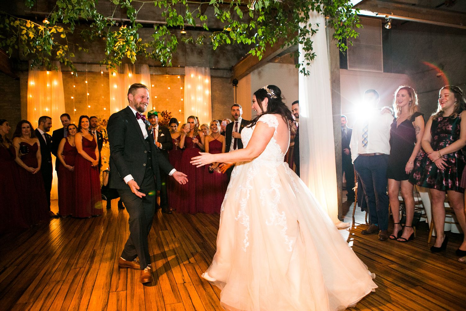 Bride and groom share first dance on wooden floor at romantic wedding reception venue.